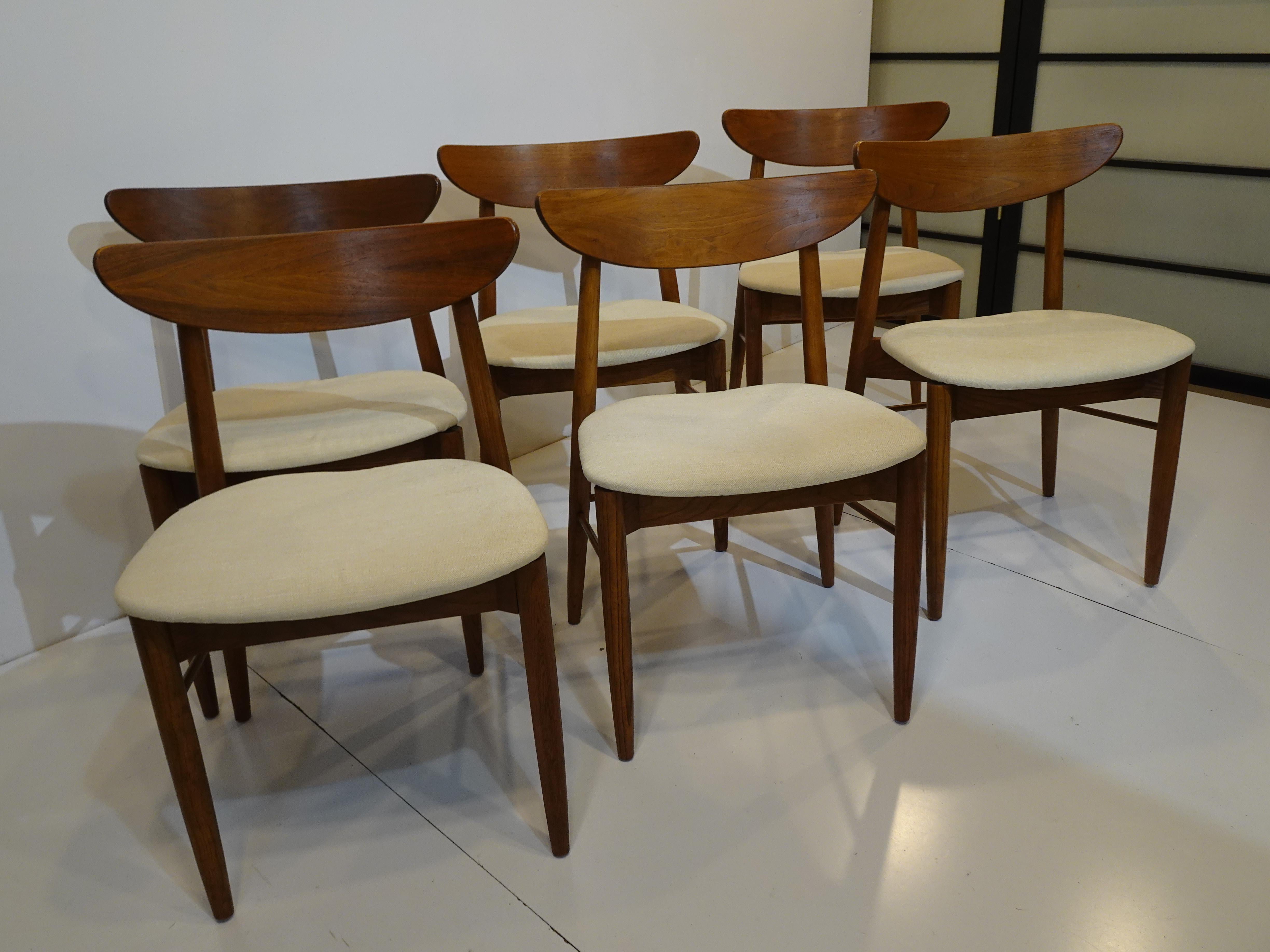 A set of six sculptural mid-century dining chairs in a medium walnut tone with cream linen contract fabric having a stylish curved backrest and X styled bracing with lower stretcher dowels. Designed by Paul Browning for the Stanley Furniture company