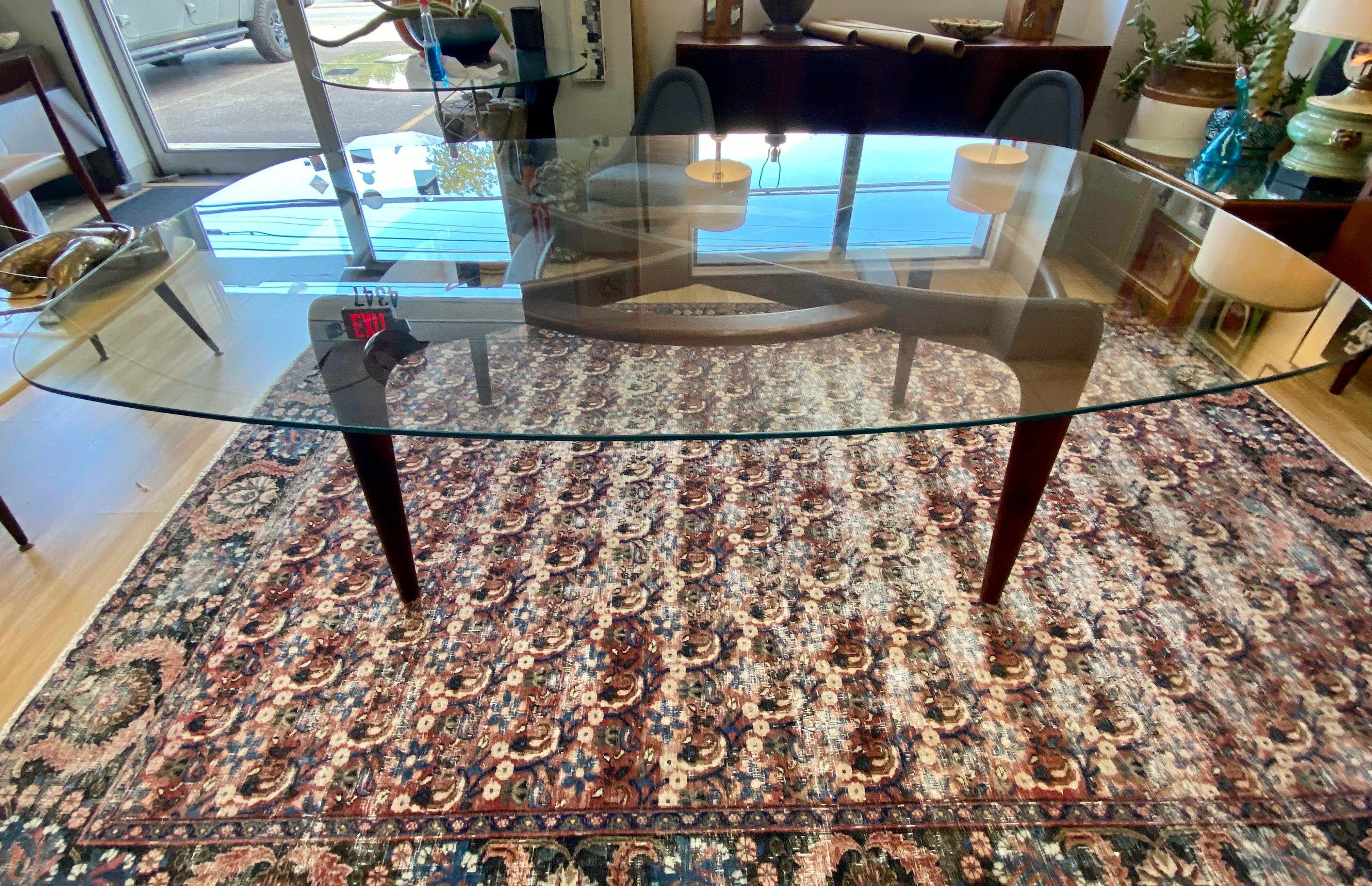 Beautiful elongated oval shaped glass top dining table by Adrian Pearsall for Craft Associates, circa 1960s. This dining table features a sculptural base made of walnut and can easily seat six. The glass measures at 82”w x 50” depth; base measures
