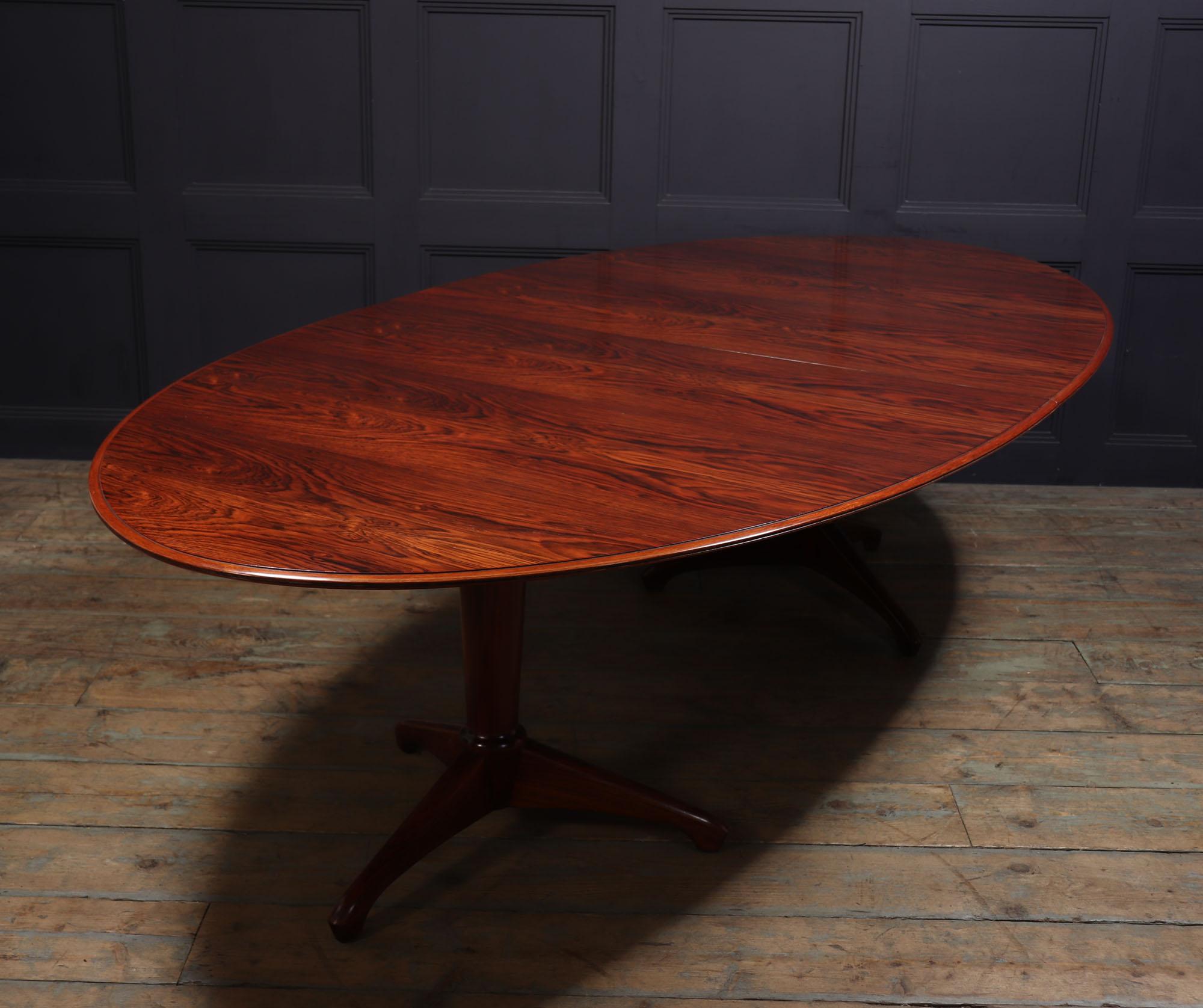 Dining table by andrew milne
A rosewood oval two pedestal extending dining table, circa 1954, the top with a moulded edge two sections consisting of on two tripod pedestal bases, with an additional central large leaf section, to comfortably seat 12