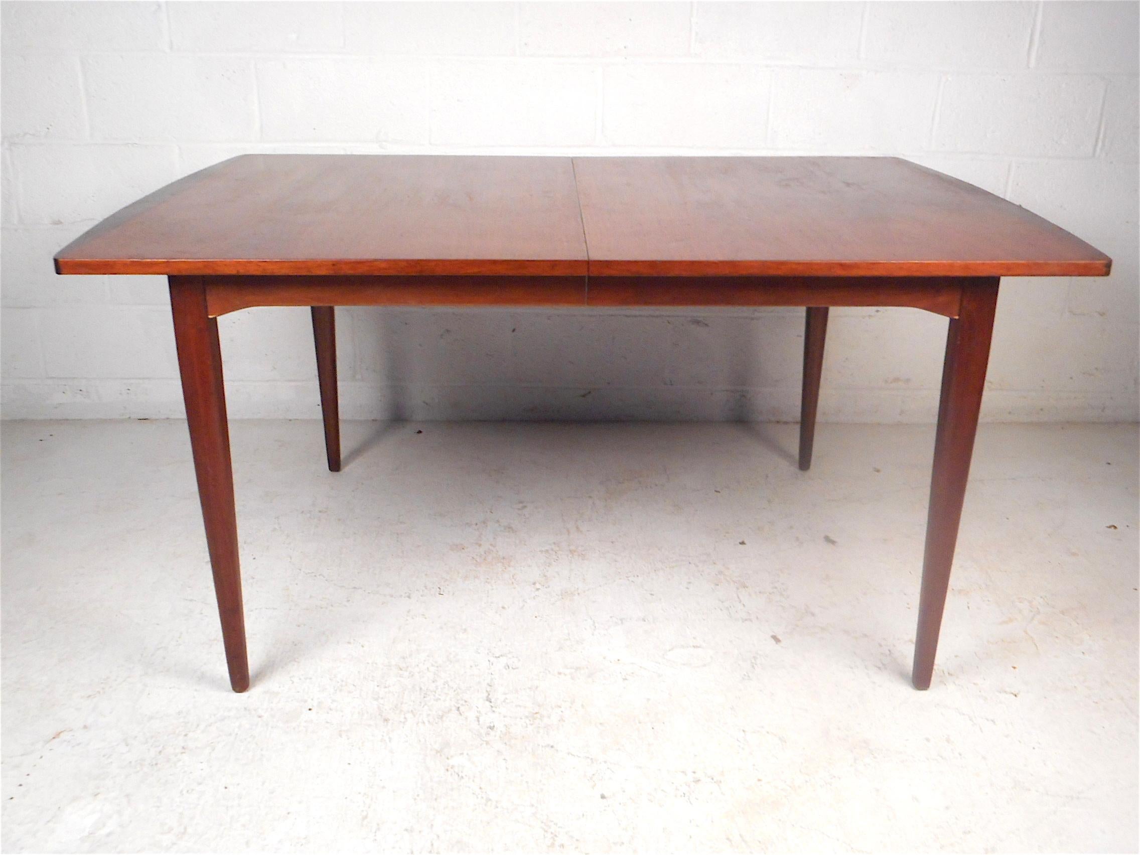 Stylish midcentury dining table made by Drexel. Sturdily made, rich walnut wood grain throughout, sleek tapered legs. Table has two leaves which expand the table's surface to accommodate additional diners. This table is sure to make a great addition