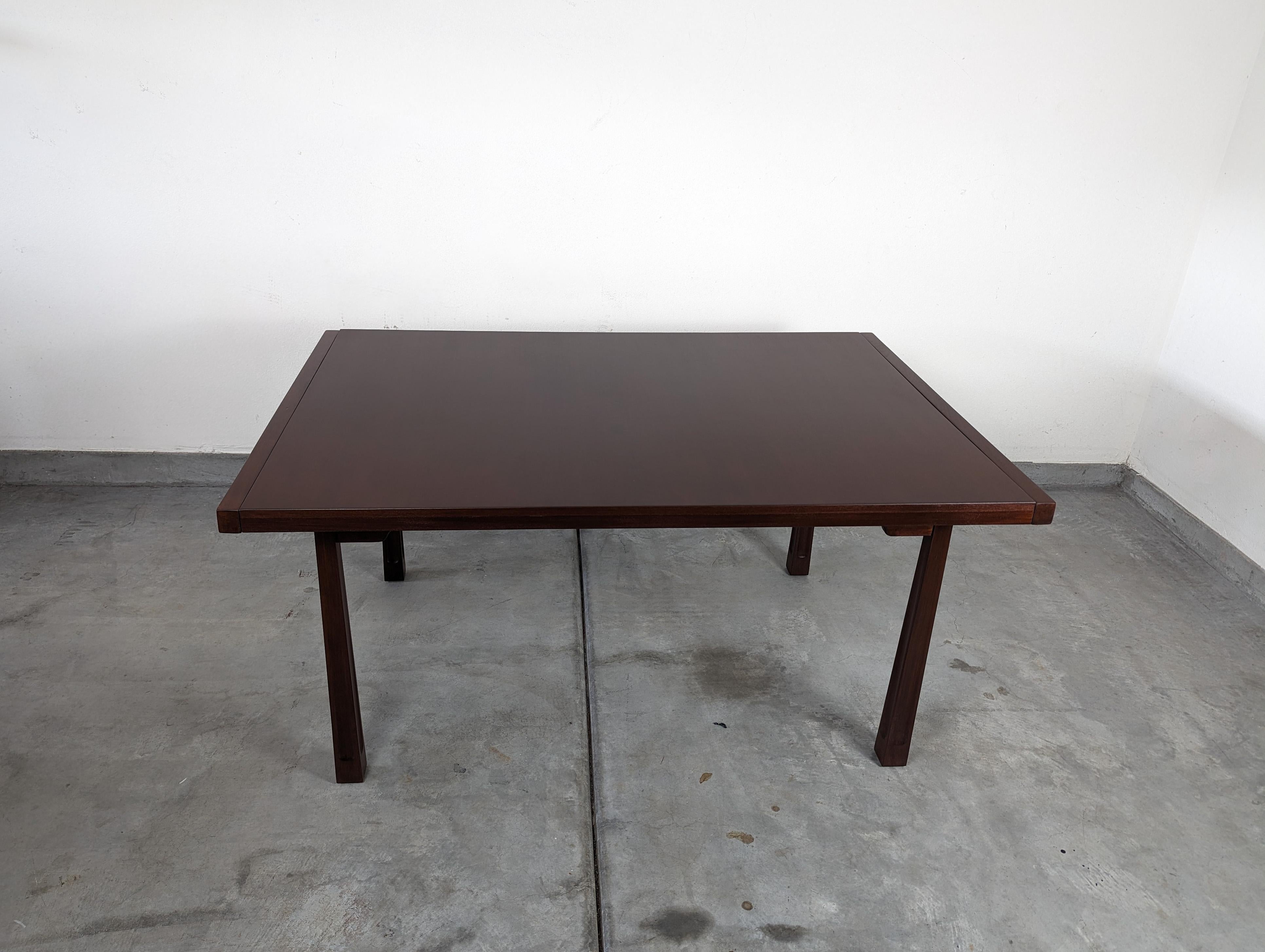 Experience a glimpse of history while dining with this stunning mid-century mahogany dining table designed by the renowned designer Edmond J. Spence and manufactured by Industria Mueblera of Mexico in the 1950s. This table showcases the perfect