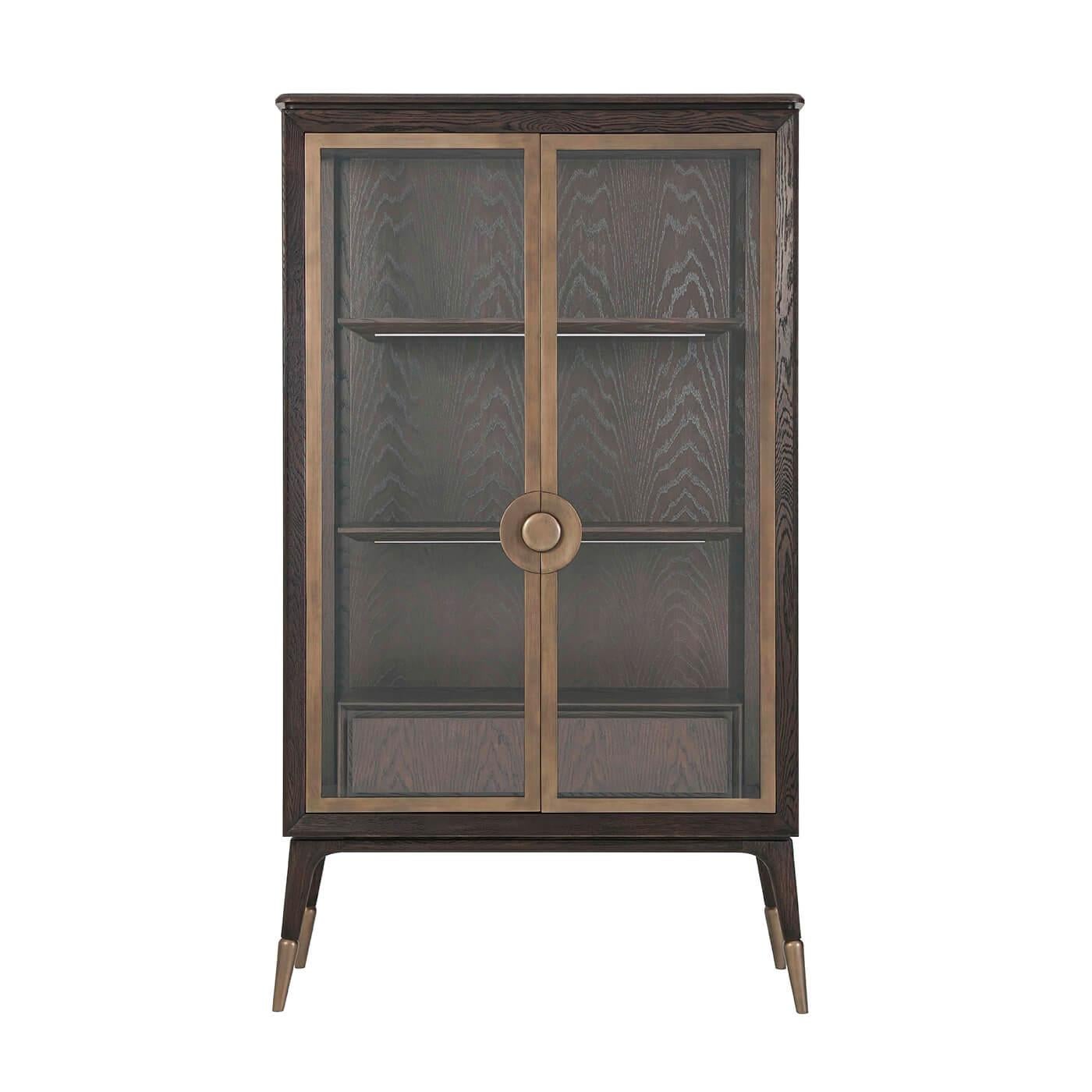 Midcentury style display cabinet with a wire-brushed oak and crown oak veneer 'cigar club' finish, glazed doors enclosing a lit interior with floating shelves and drawer box, our 'Heritage Bronze' finished legs, handle and door frame on splayed legs