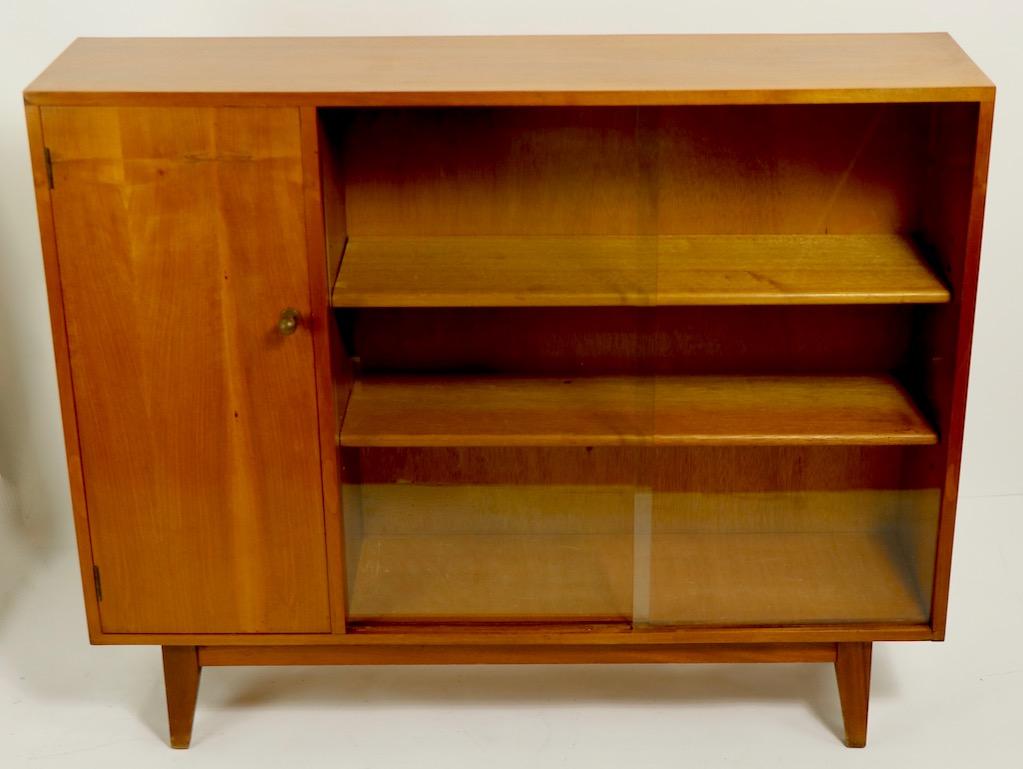 Chic and sophisticated display case, made by respected English furniture maker Gimson and Slater. The case features sliding glass doors which open to adjustable wood shelves, flanked by a wood door which open to more shelved storage space. 
 Total