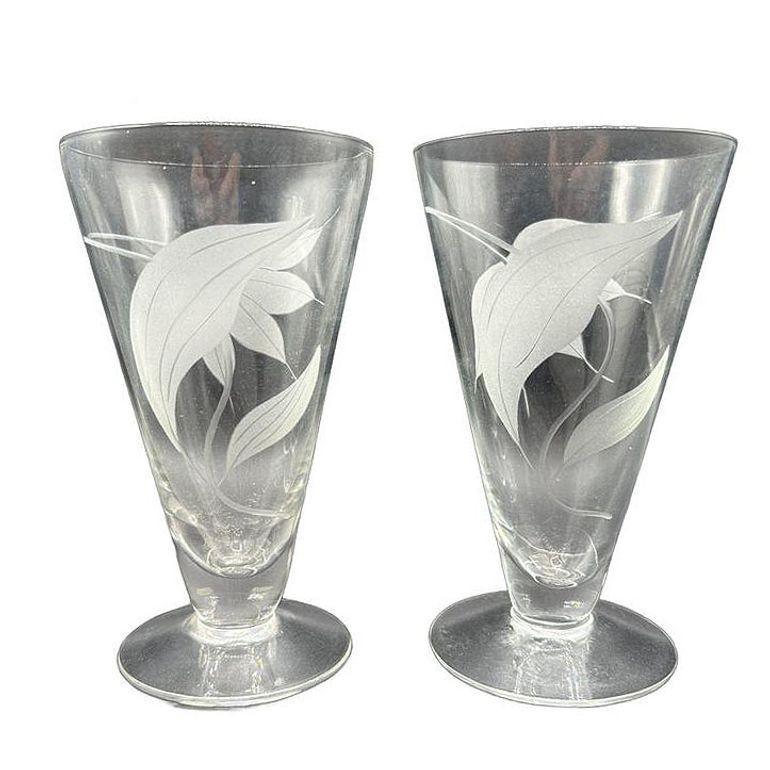Attribuita allo stile di Dorothy Thorpe, questa coppia di tumbler con piede presenta un elegante disegno inciso di gigli tropicali esotici e motivi botanici. Entrambi gli occhiali sono caratterizzati dall'iconico minimalismo di Thorpe, con una