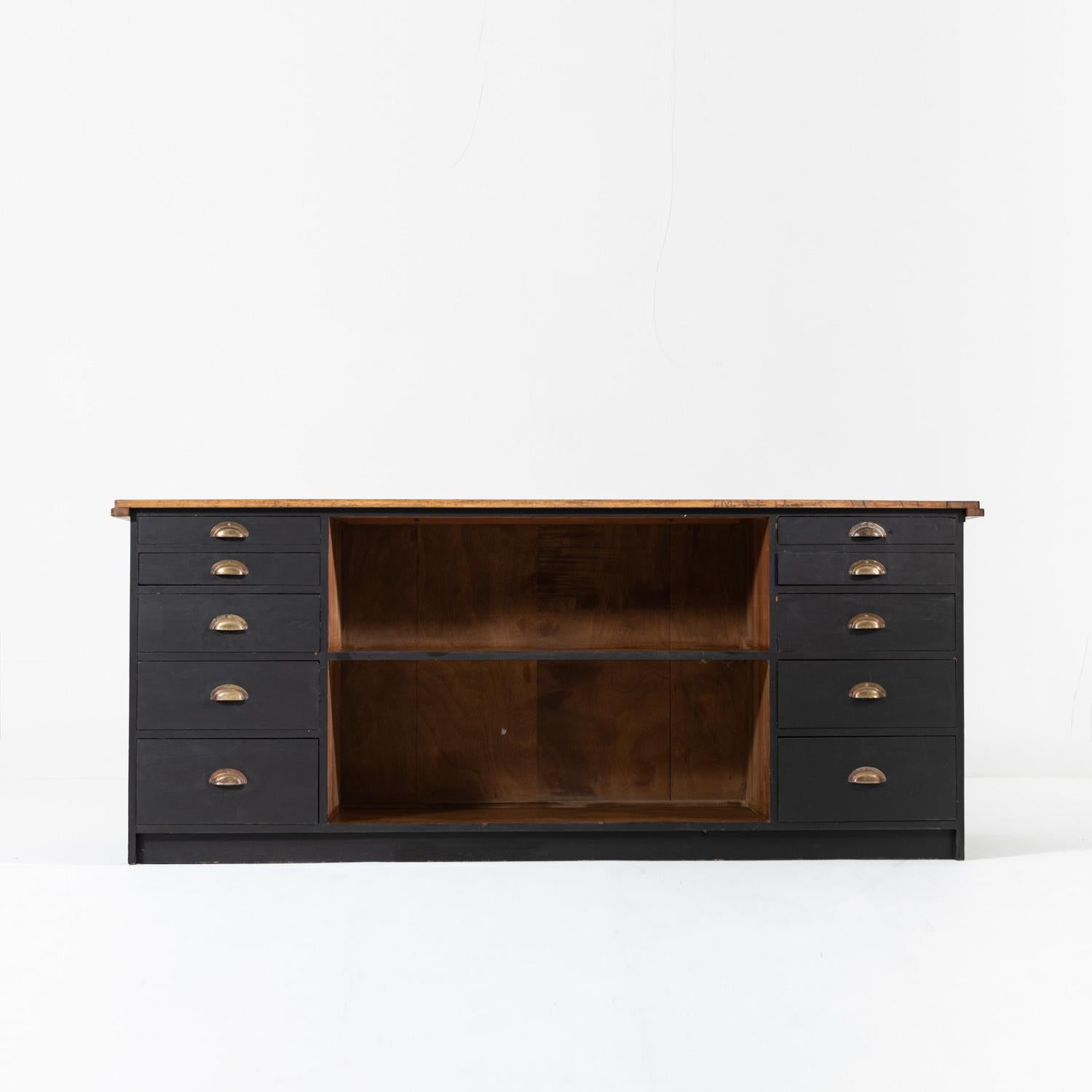 Sturdy midcentury double sided painted oak shop counter.

The piece has abundant storage with sliding glass doors opening to shelves at the front, whilst the back has two banks of five drawers on either side of a large open shelf.

This piece