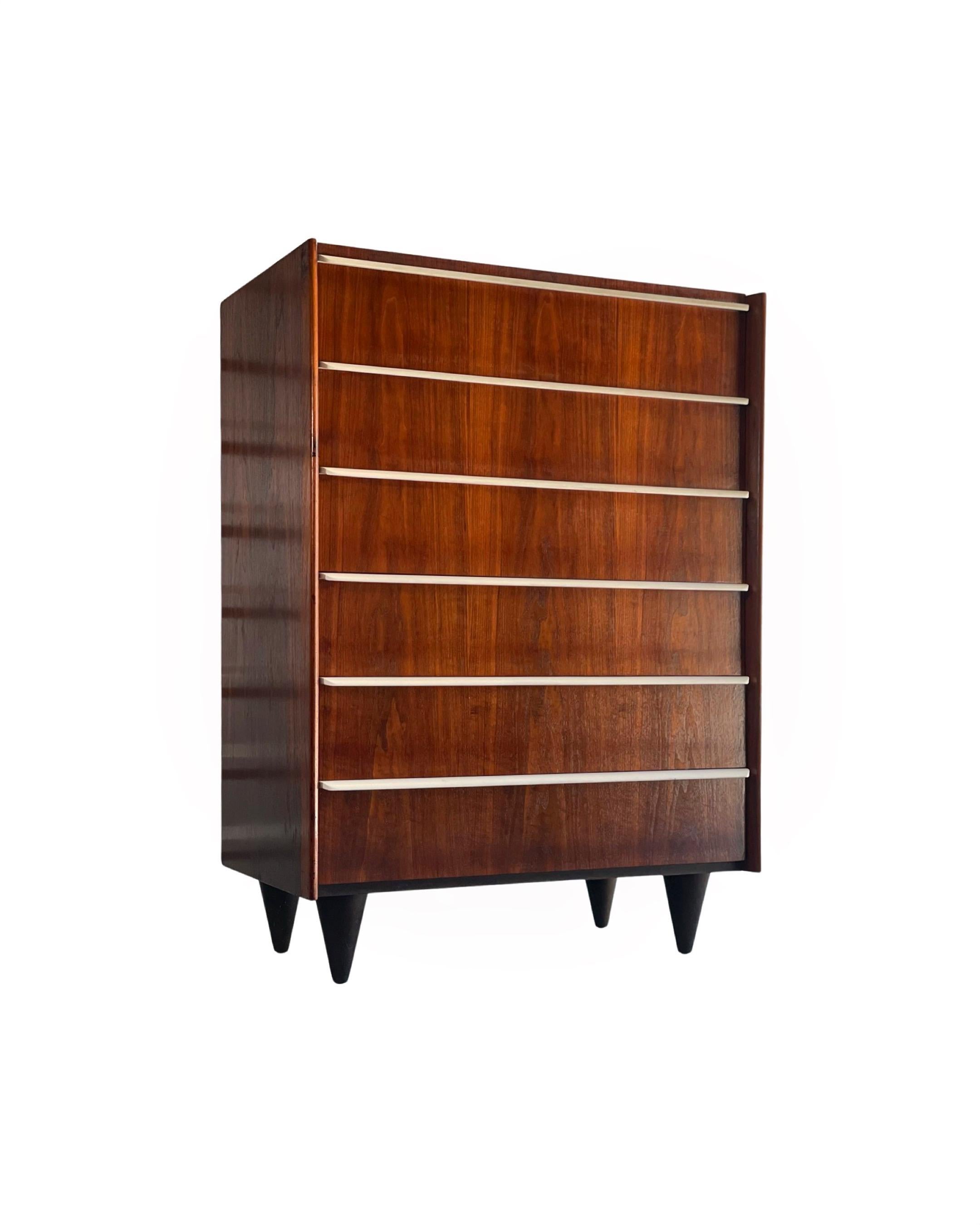 Rare six drawer tall chest by Gilbert Rohde for Herman Miller, circa 1948. Cathedral book matched walnut grain on the drawer facades juxtaposed with original creamy white drawer pulls. Hard to find example of Rohde's transition to more a modern