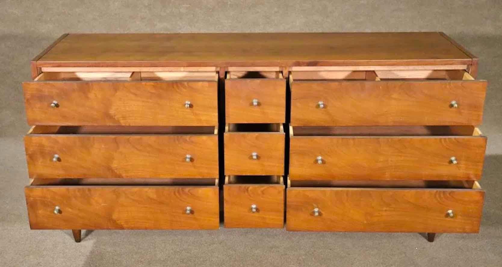 Long Mid-Century Modern dresser with nine drawers. Metal drawer pulls and walnut wood grain.
Please confirm location.