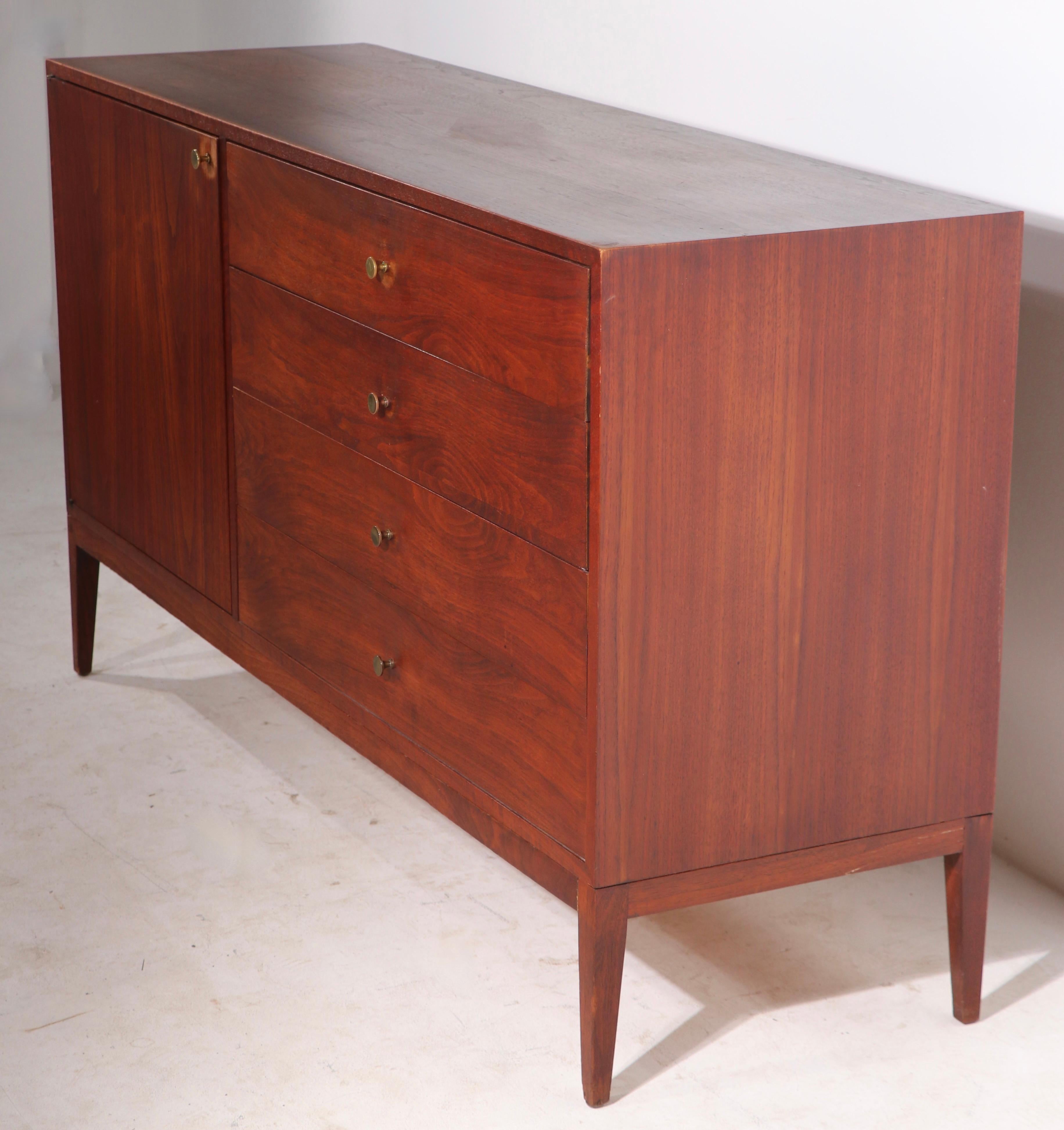 Well constructed mid-century cabinet of solid walnut, walnut veneer, and brass. The case features a bi - fold door which opens to 4 interior drawers, flanked by a bank of 4 drawers with brass pulls. The dresser is structurally sound and sturdy, the