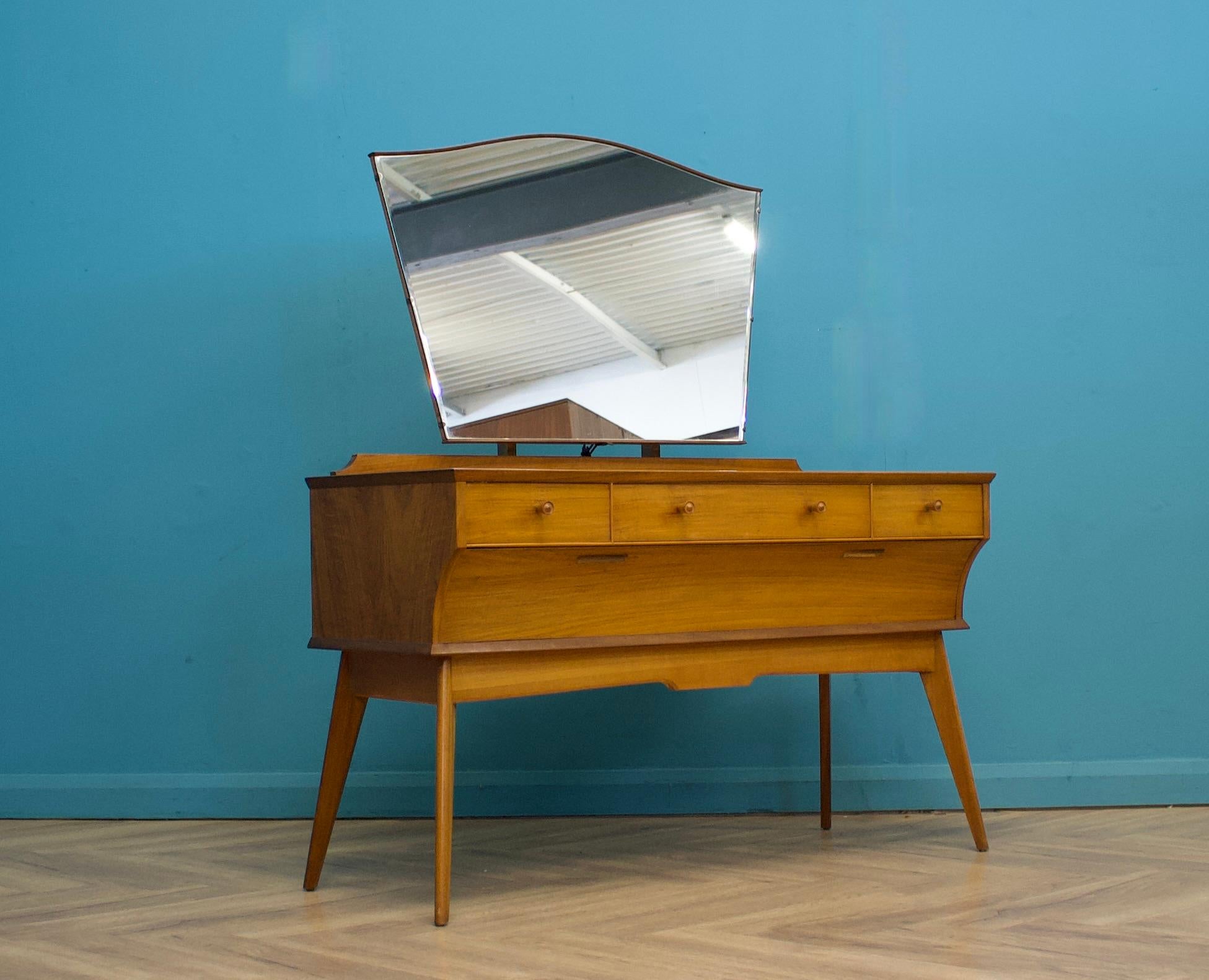 A mid-century walnut dressing table from Alfred Cox, circa 1950s.
These pieces were usually retailed through Heals


The dressing table includes three drawers to the top and a concealed larger drawer to the bottom.
Featuring a central