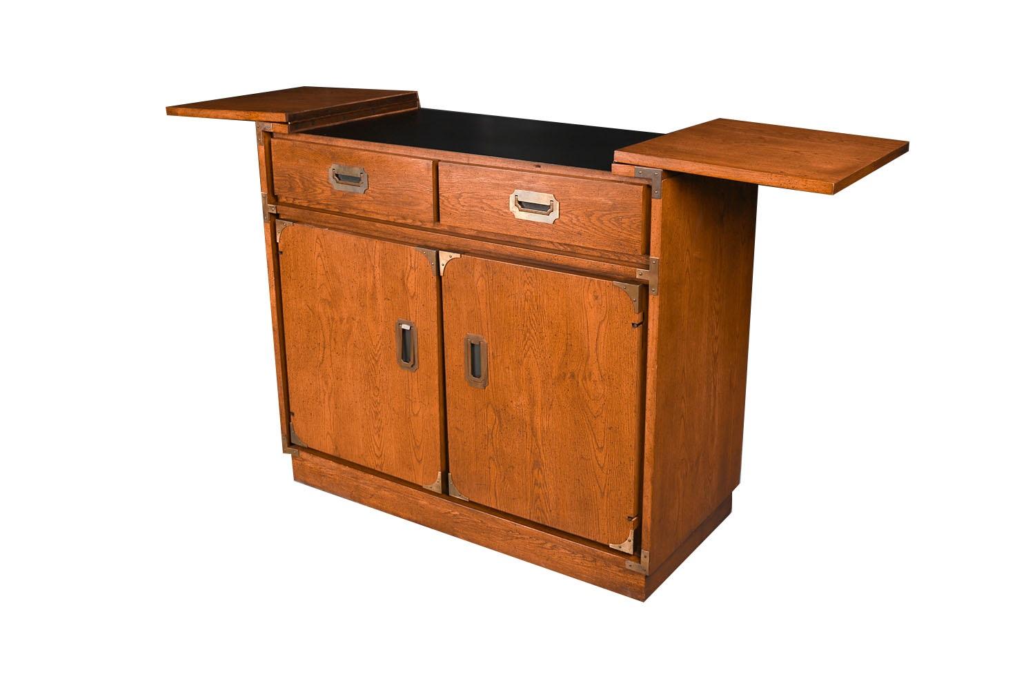 Mid-century campaign style console bar cabinet is an excellent example of mid-century modern. Minimalist Danish Modern inspired profile, with exceptional construction and style and adorned with original stylish, sculpted, brass pulls.  Featuring