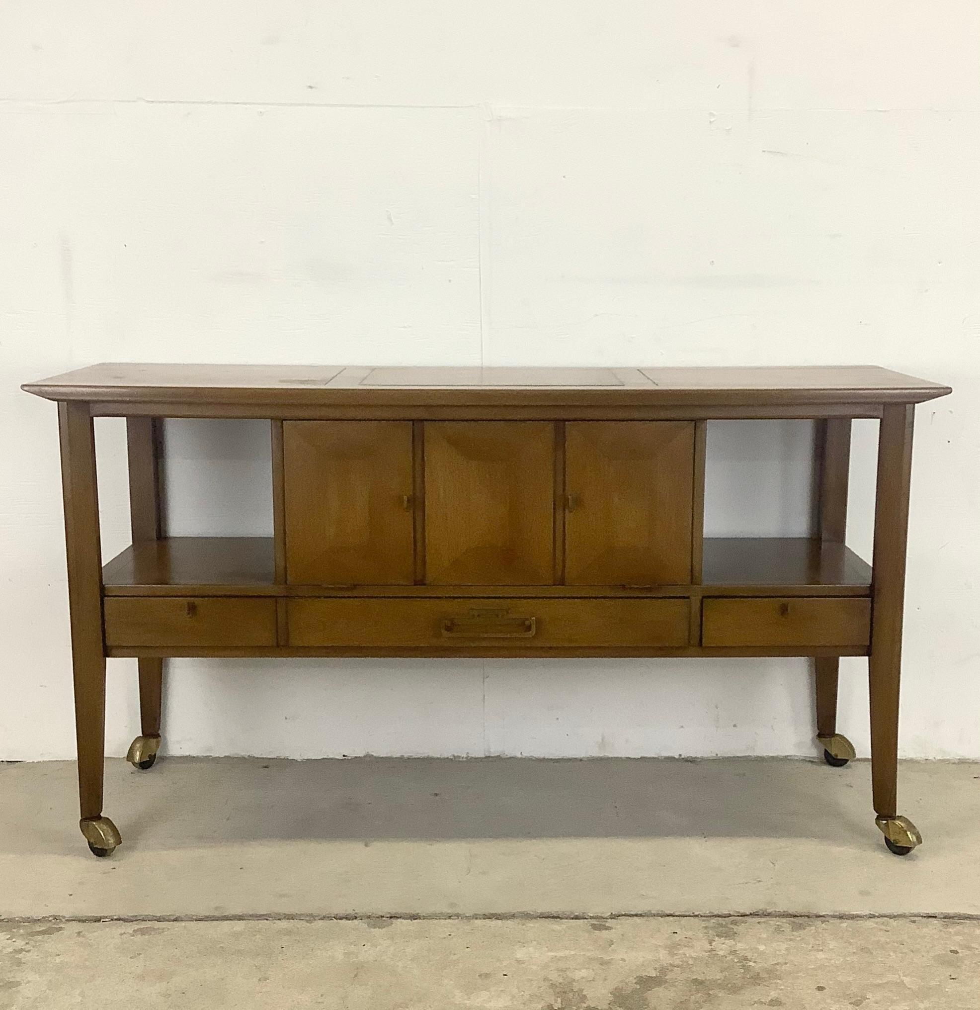 This unique mid-century service cart from White Furniture features beautiful vintage walnut finish combined with brass trim pulls and spacious storage options. The drop front cabinet storage pairs perfectly with additional drawers and shelf space