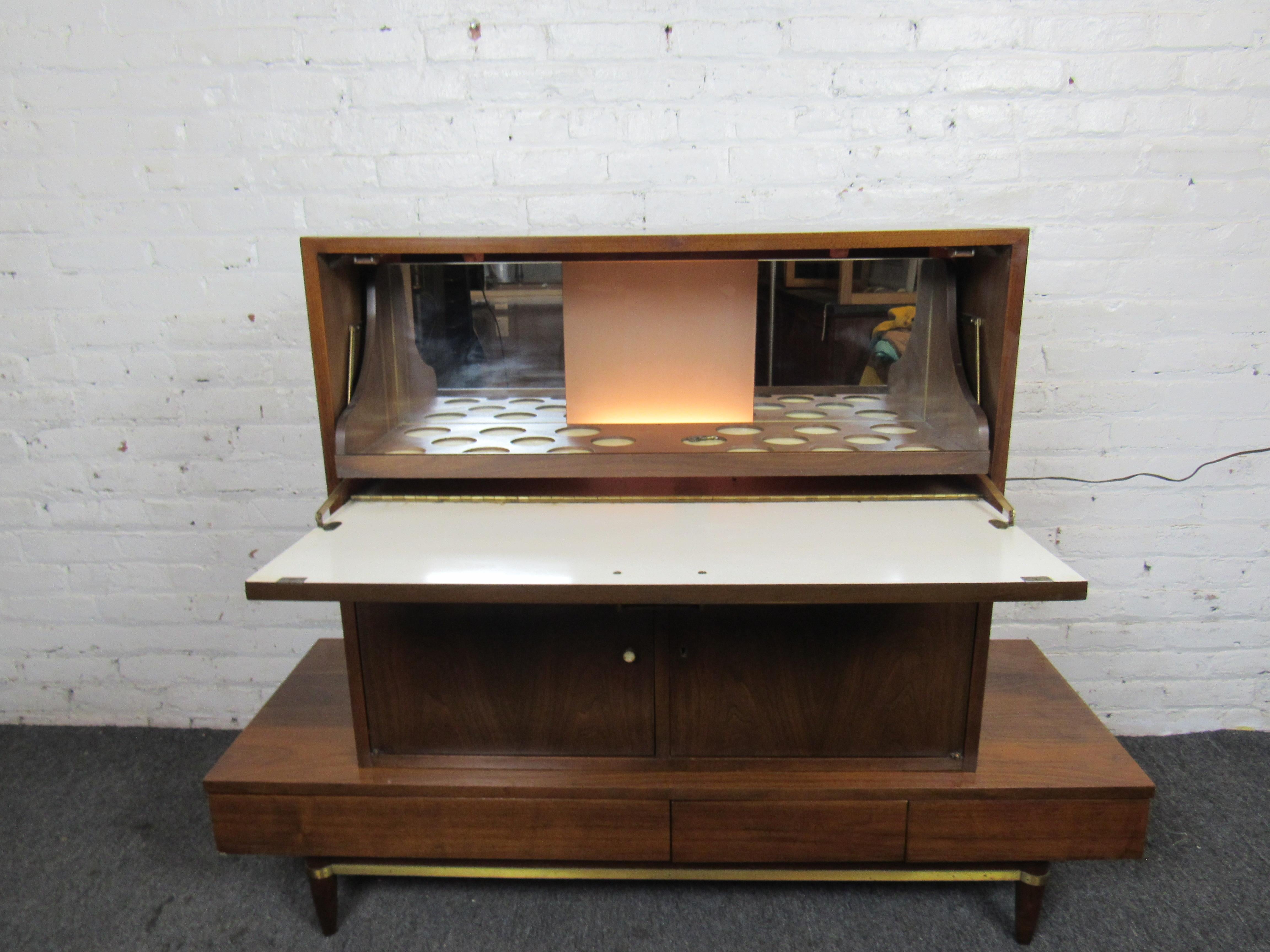 This incredible dry bar cabinet by Martinsville is a Mid-Century Modern gem, with a large top compartment that lights up with holders for drinks. A lower storage compartment and slide out drawers at the bottom allow for storage and organization of