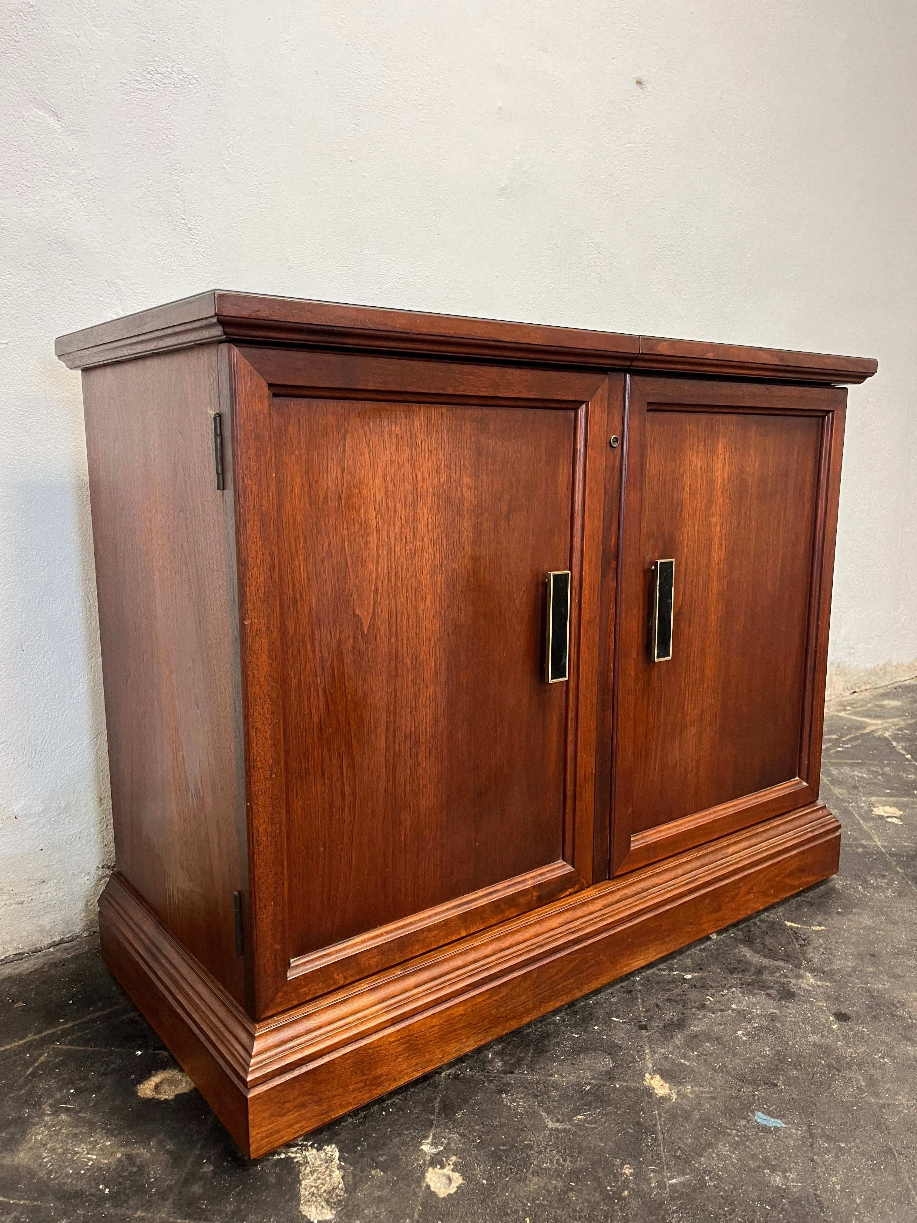 Sophisticated Mid Century Dry Bar with expandable top. Beautiful walnut case topped with sliding protected coated top surface to expose tiered shelving. Deep and tall storage, built in glass and wine rack. Interior lighting illuminates top shelf.