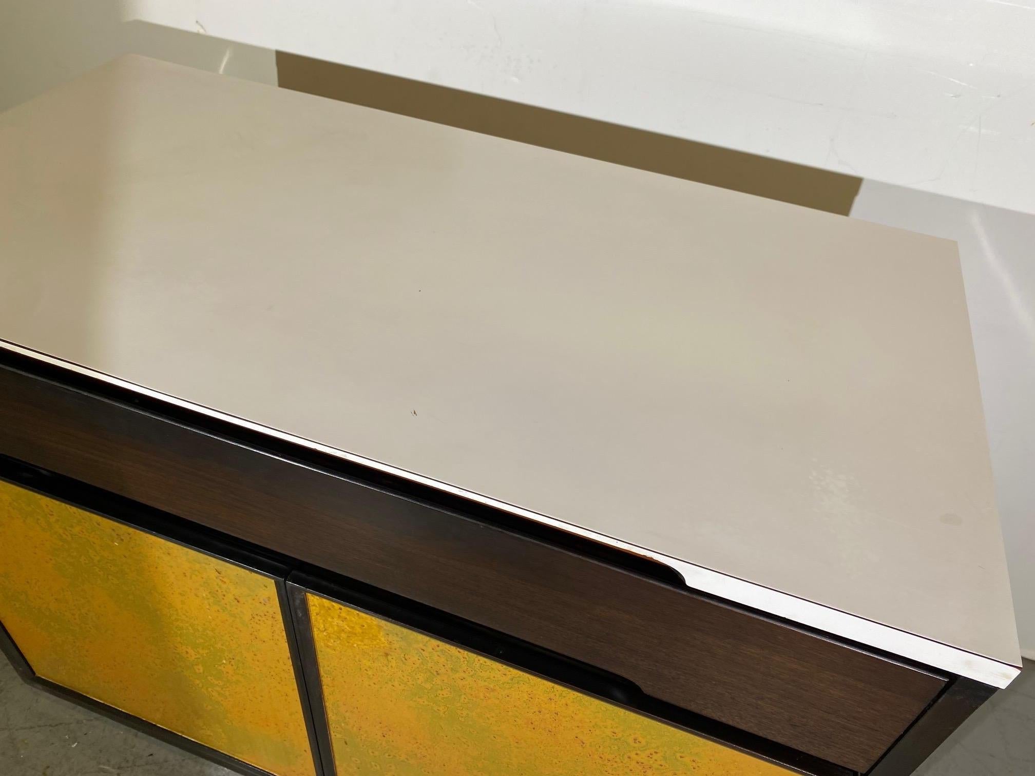 Un bar sec du milieu du siècle. Le plateau est en vinyle blanc, le tiroir est en bois de rose et le couvercle inférieur est doté d'une étagère simple réglable.