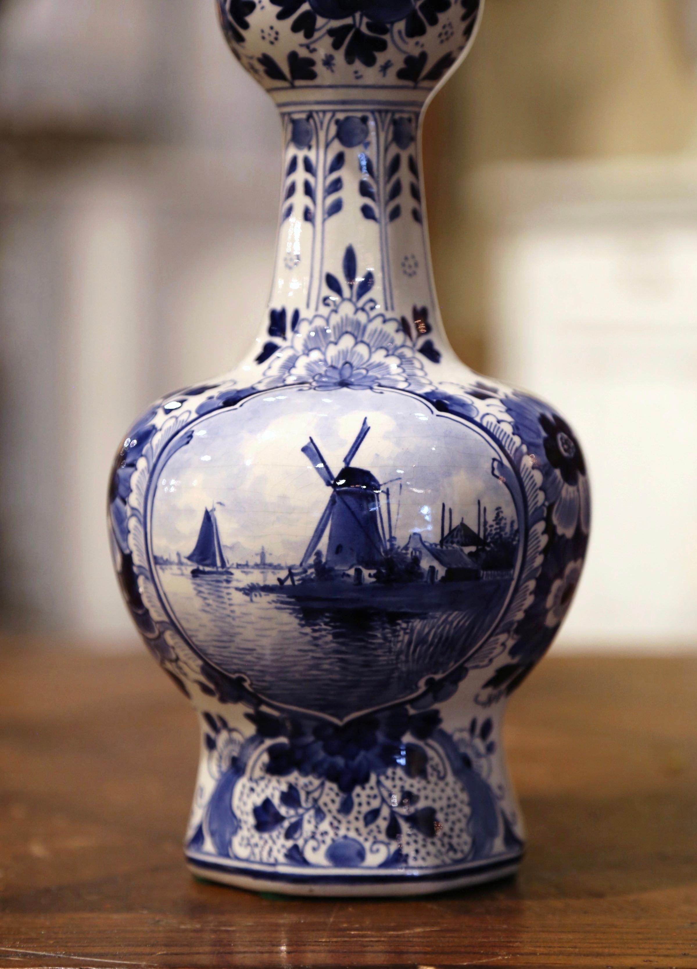 Decorate a shelf or console table with this elegant and colorful antique Delft vase. Crafted in Holland circa 1950, the flower holder is round in shape over an elegant neck. The vessel is hand painted in the traditional blue and white Delft palette,