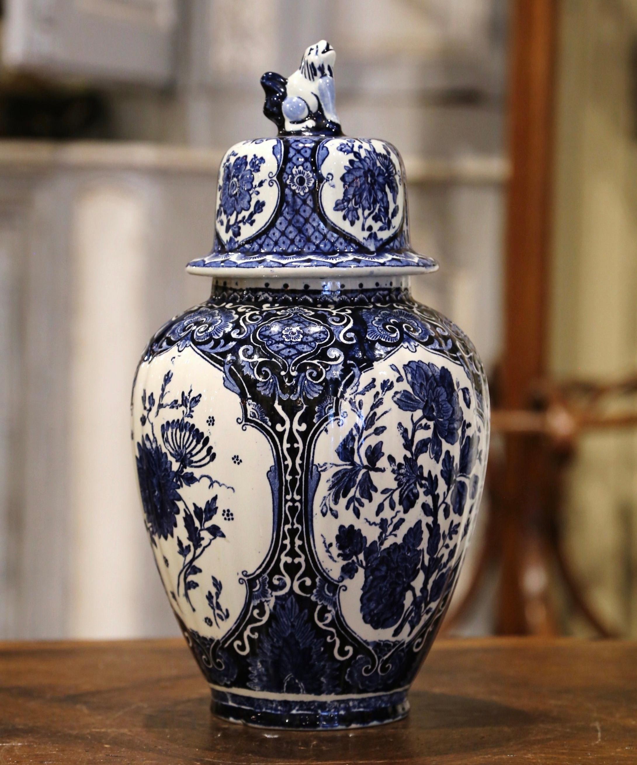 Crafted in Holland, circa 1940, the large faience potiche features hand painted medallions with Classic Dutch flower and foliage decor. The traditional blue and white jar is round in shape and has a cone lid embellished with dog figure at the top.