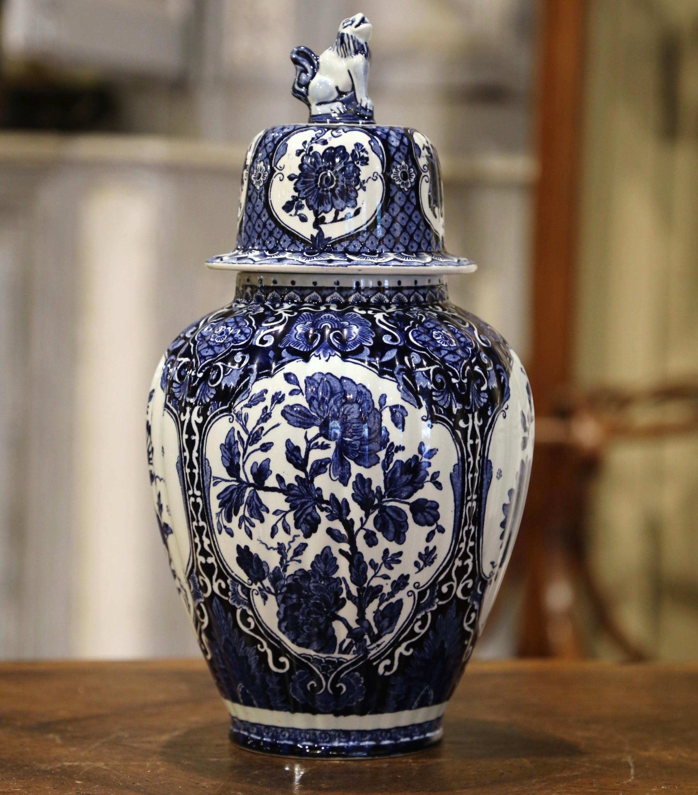 Crafted in Holland, circa 1940, the large faience potiche features hand painted medallions with Classic Dutch flower and foliage decor. The traditional blue and white jar is round in shape and has a cone lid embellished with dog figure at the top.