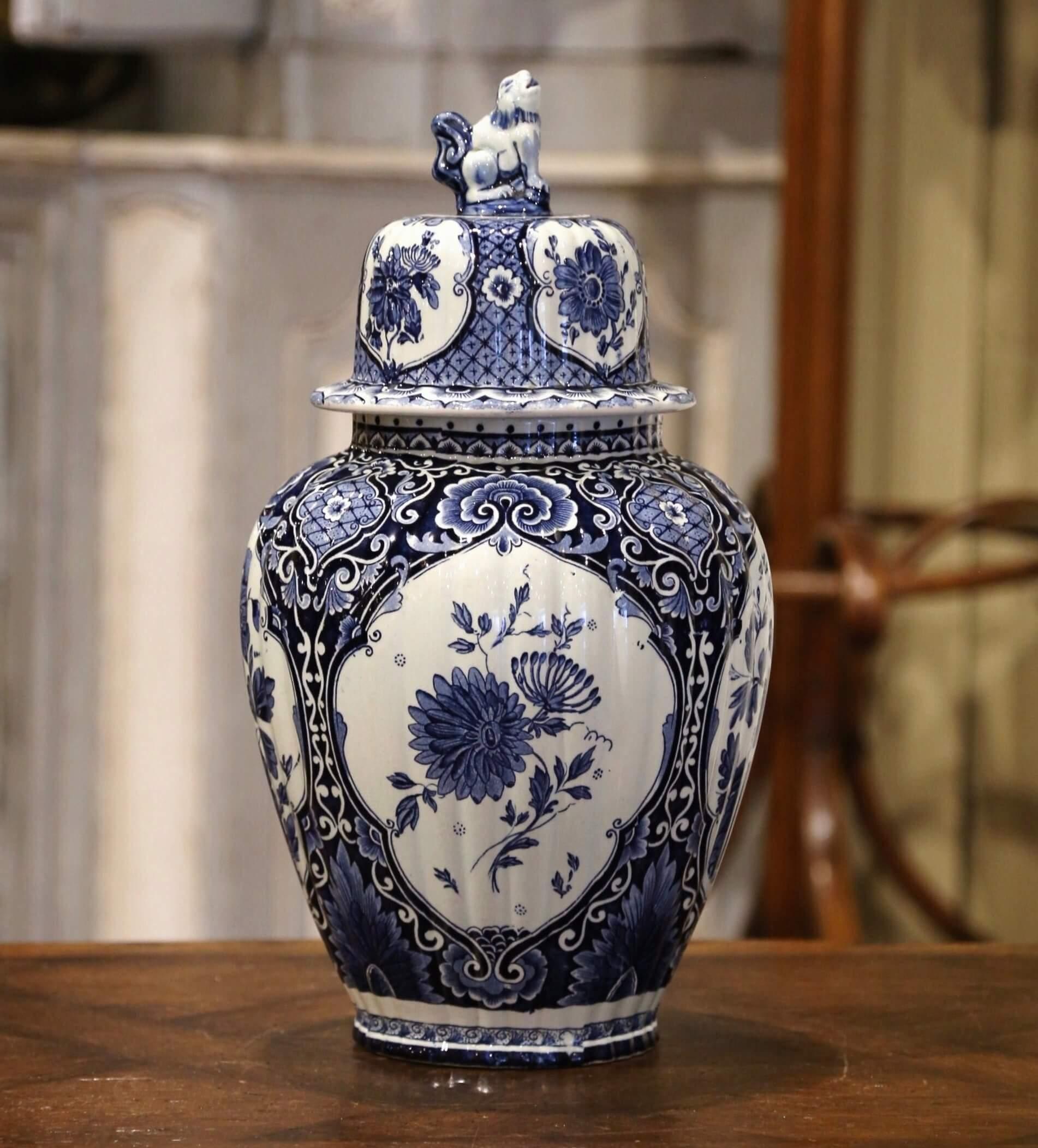 Crafted in Holland, circa 1950, the large faience potiche features hand painted medallions with Classic Dutch flower and foliage decor. The traditional blue and white jar is round in shape and has a cone lid embellished with dog figure at the top.