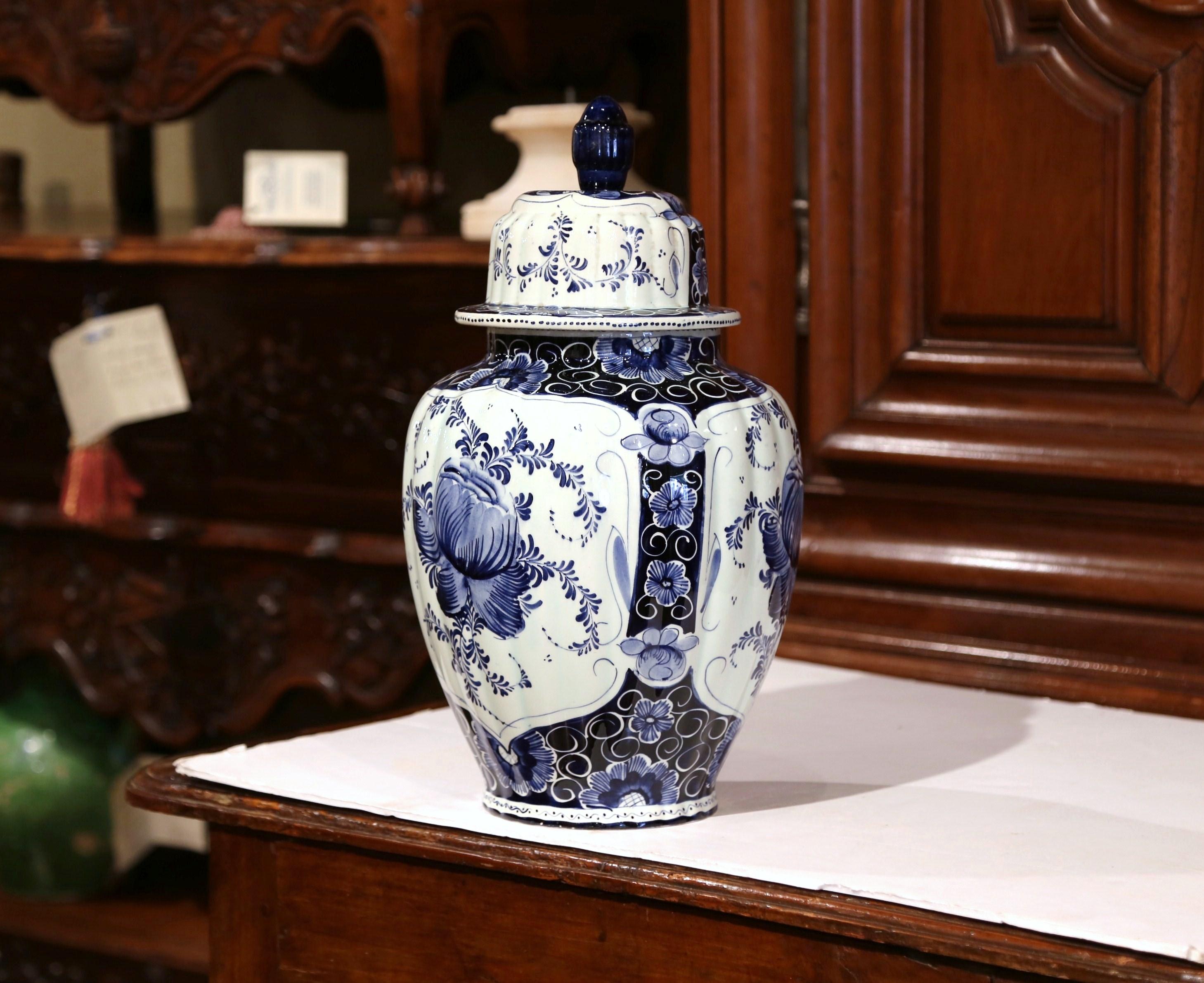 This large round ginger jar was created in Holland, circa 1960. The porcelain vase with dome shaped lid and top finial, features hand painted floral decor in the traditional blue and white palette. The ceramic piece is in excellent condition with