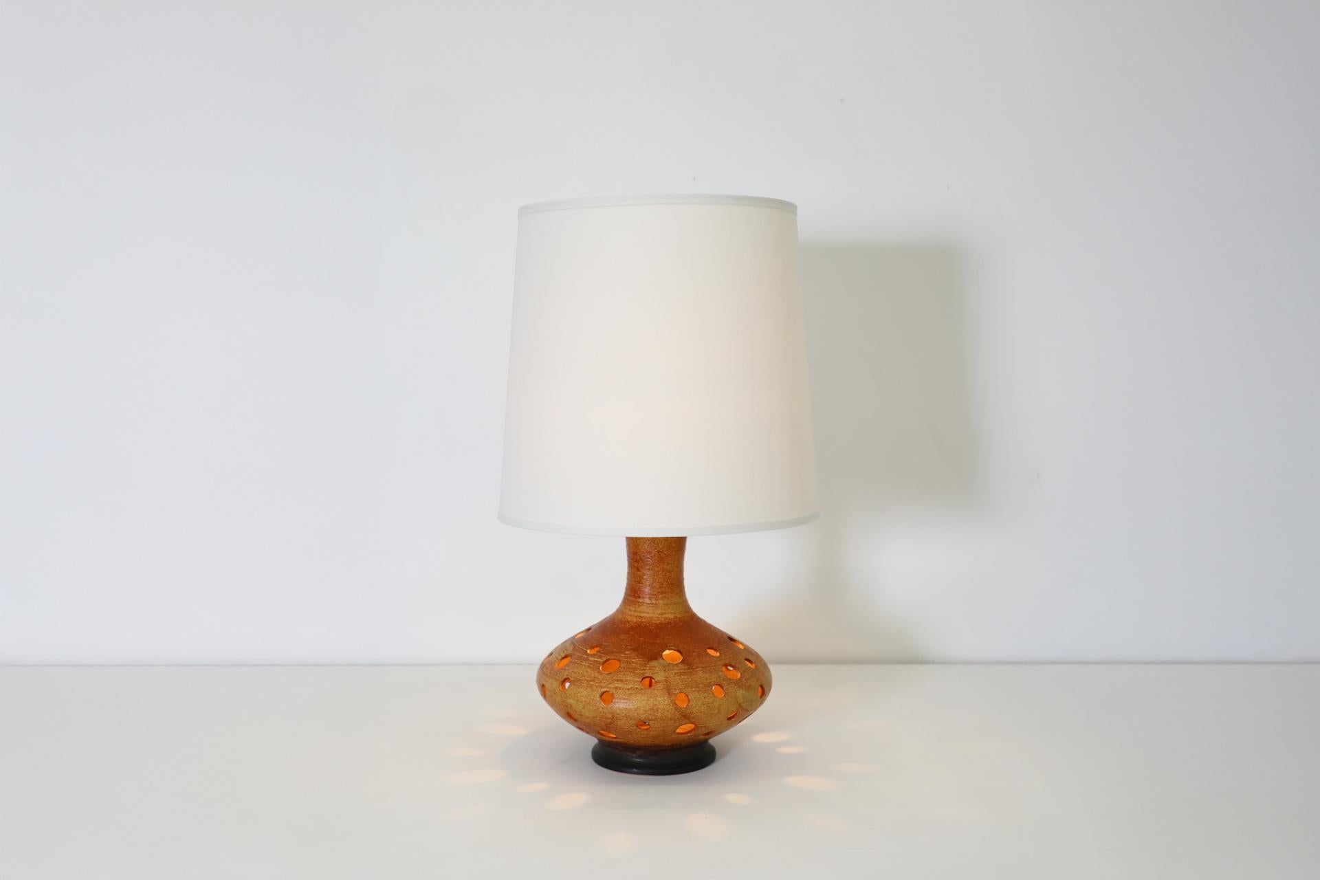 Lámpara de sobremesa holandesa de mediados de siglo, de cerámica esmaltada naranja con recortes redondos. Esta lámpara tiene una bombilla normal de base mediana que sirve como fuente de luz principal y una bombilla candelabro UE en su interior que