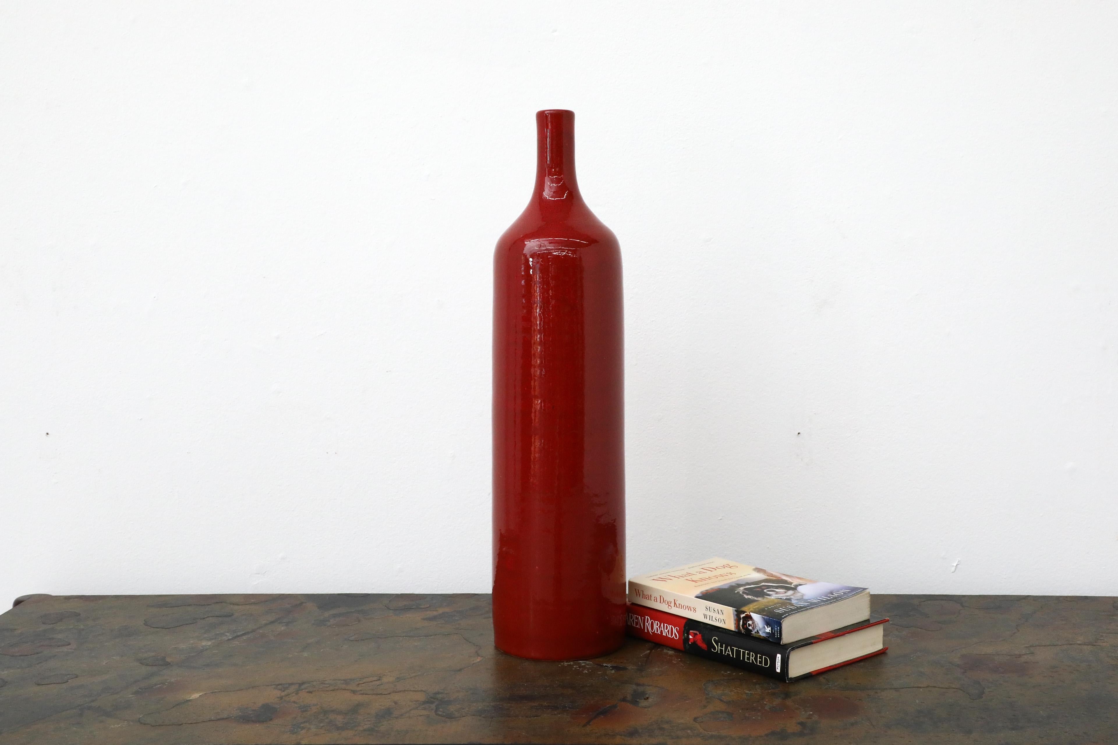Precioso jarrón de cerámica roja con forma de botella de vino. Este jarrón es muy alto con un esmalte moteado brillante y tiene una pequeña abertura en la parte superior, perfecta para unas cuantas flores de tallo largo. En estado original con
