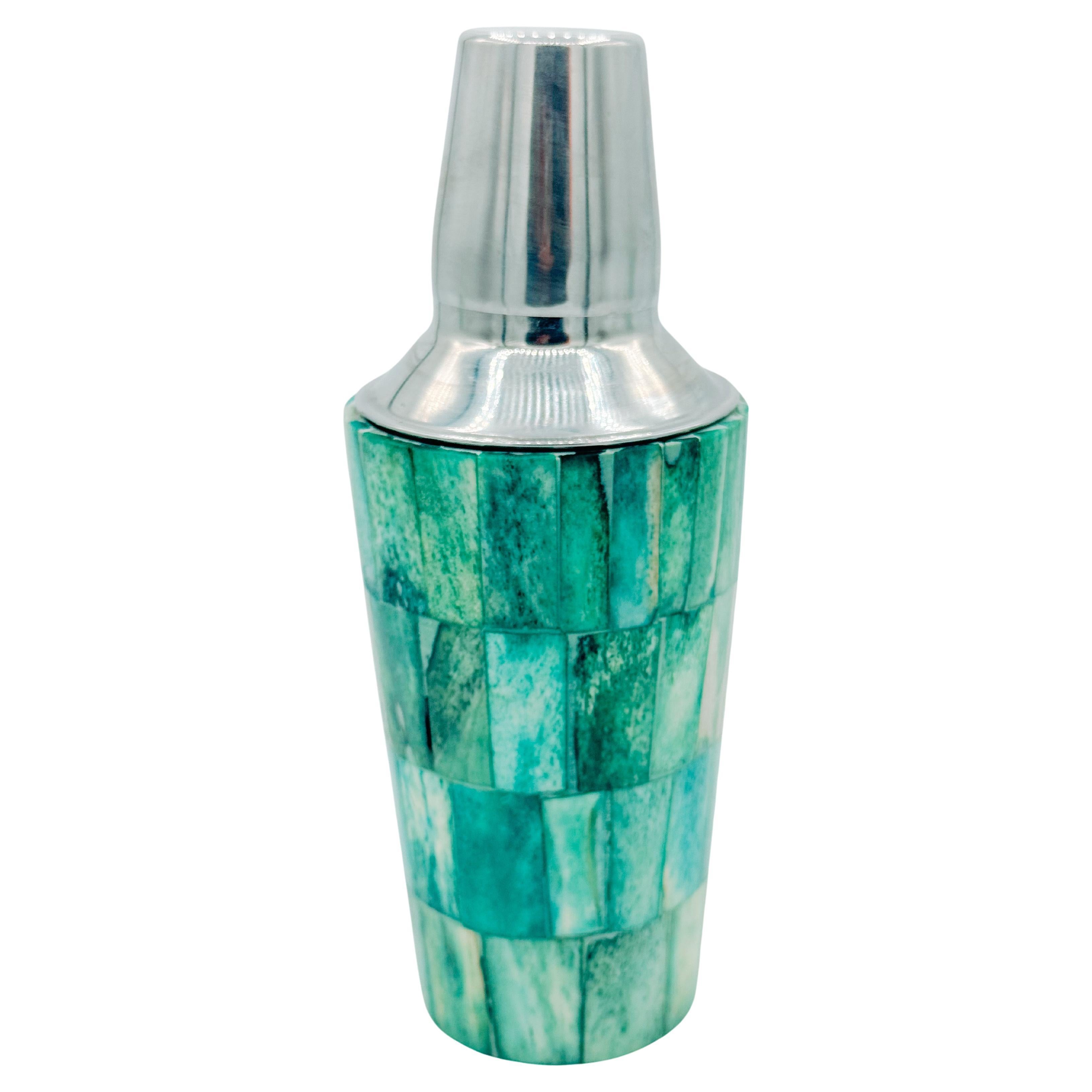 This vibrant mid-century cocktail shaker features a beautifully tiled mosaic body made of dyed wood in shades of turquoise, jade, and seafoam green. The geometric pattern wraps around the shaker with a smooth, tactile finish, creating a piece that’s