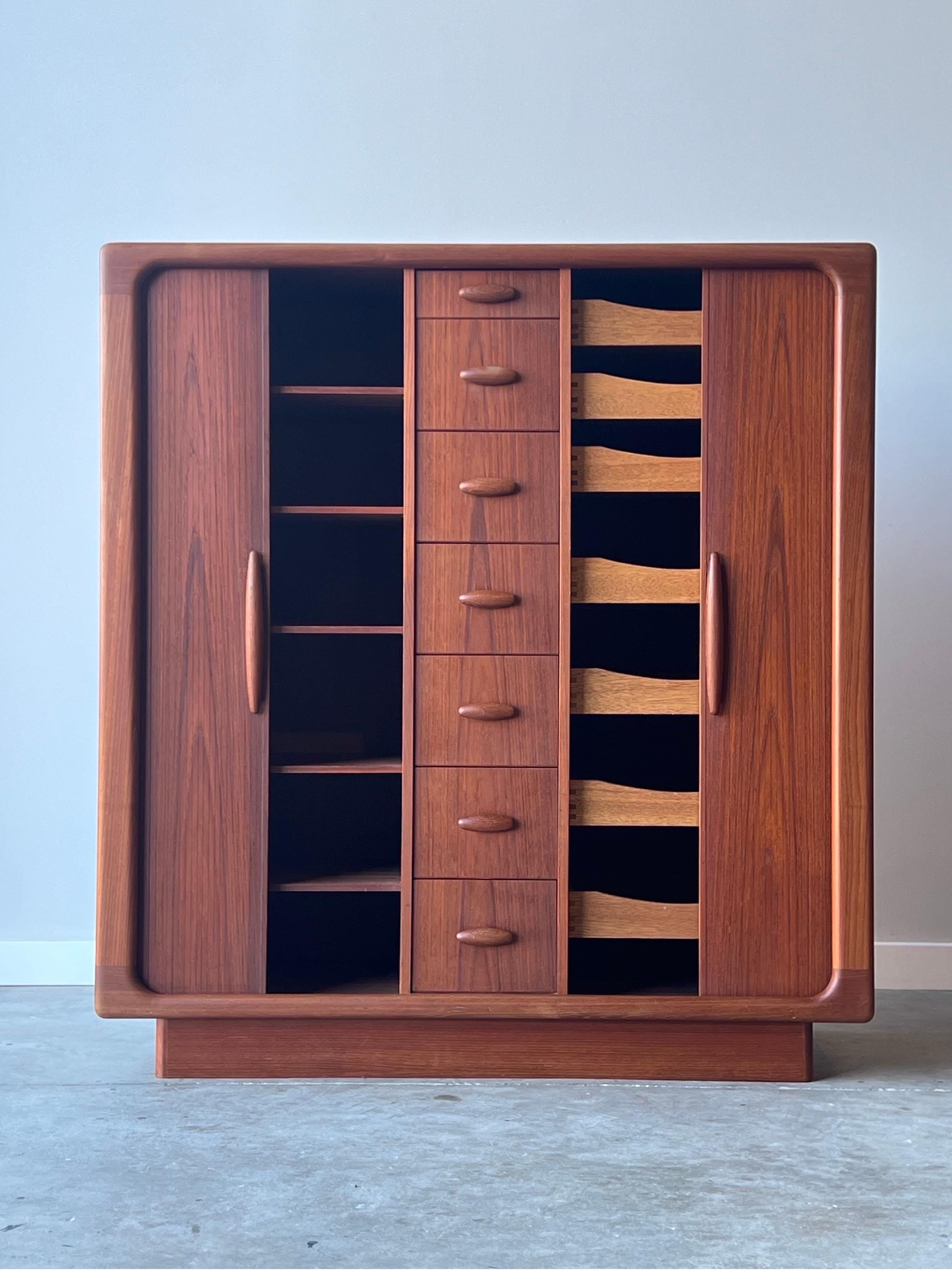 Massive mid-century highboy / armoire by Dyrlund, Denmark. This tall dresser is made from beautifully sculpted teak wood, circa 1970s. Two tambour doors on both the left and right side of the dresser. The middle section is home to seven smooth