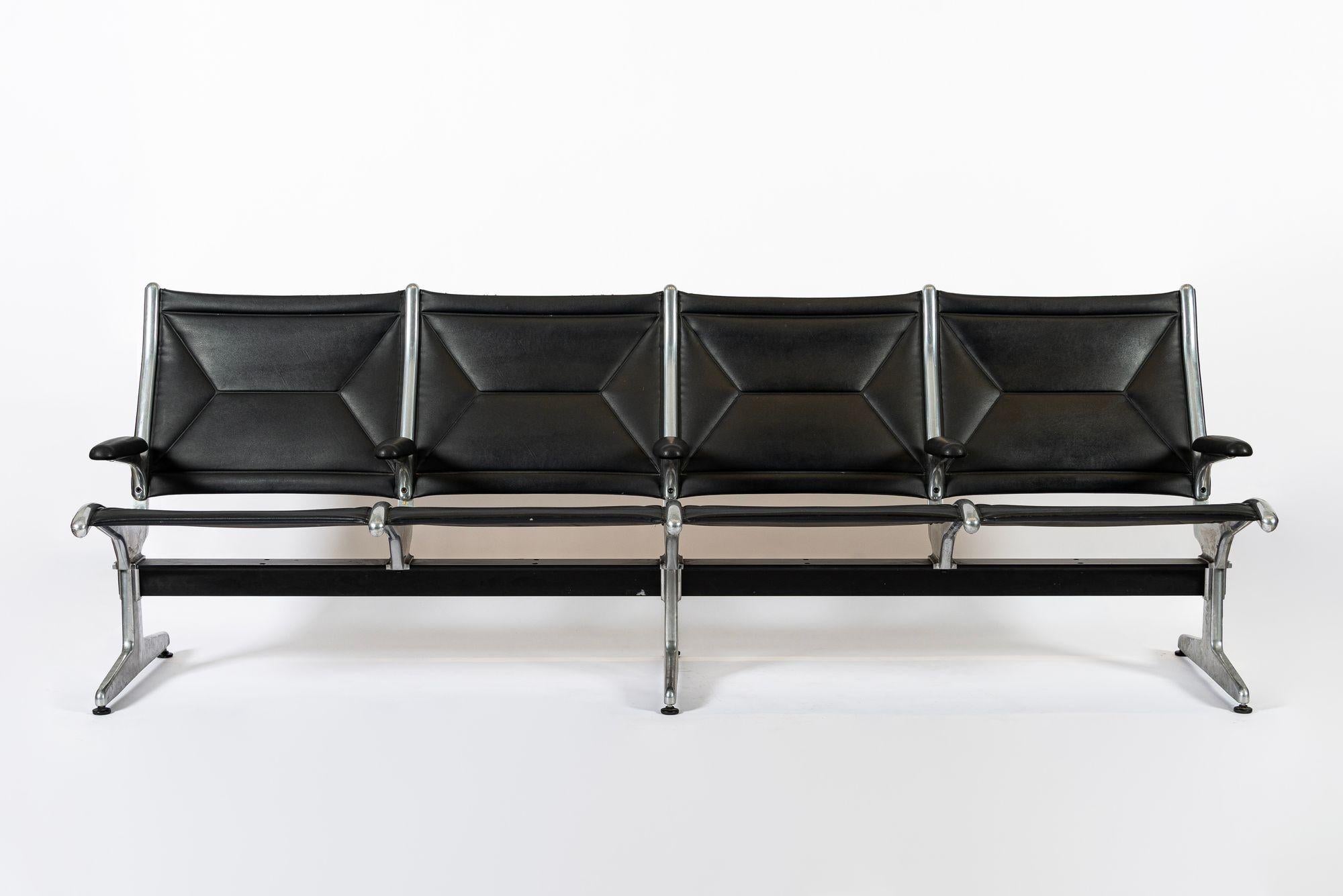 Questo classico sedile a fionda tandem Eames della metà del secolo scorso risale al 1990. Questo set indipendente presenta una configurazione a quattro posti con sedute sospese in tessuto Naugahyde nero originale e una pesante struttura in alluminio