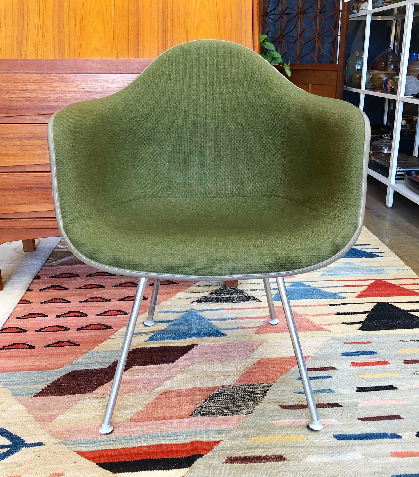 A mid century molded fiberglass armchair by Charles and Ray Eames for Herman Miller. Features an upholstered interior with a woven avocado green fabric. The fiberglass shell is a light beige color. Stands on a 4 metal leg base. Stamped by Herman