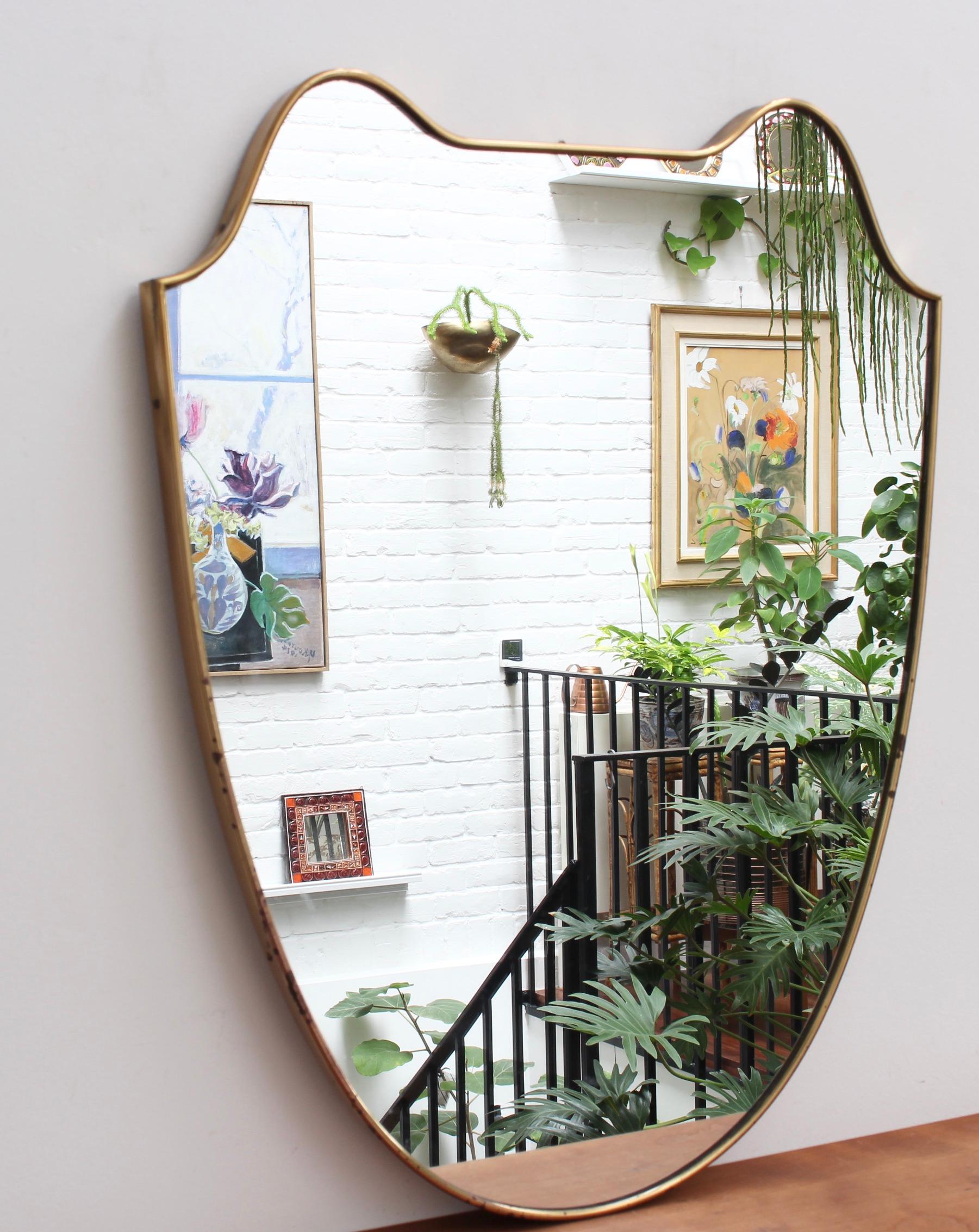 Vintage Italian wall mirror with brass frame, (circa 1950s). The crest-shaped mirror is substantial with sensuous curves crowning the piece. It exudes character, solidity, weightiness and has eye-catching good looks. Two 'ears' give the mirror a