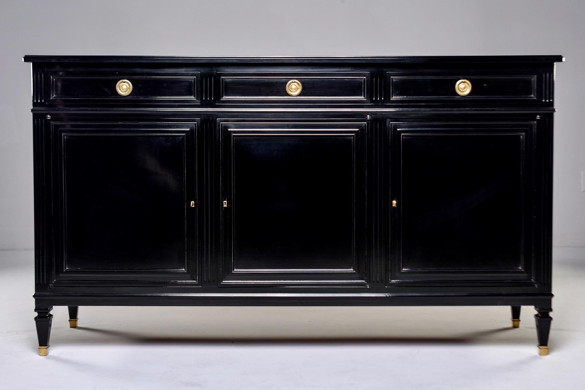 Found in England, this circa 1950s mahogany commode or buffet has a new ebonized finish. At the top are three narrow drawers with dovetail construction and three locking hinged door cabinets below. Each cabinet has one adjustable shelf. Brass