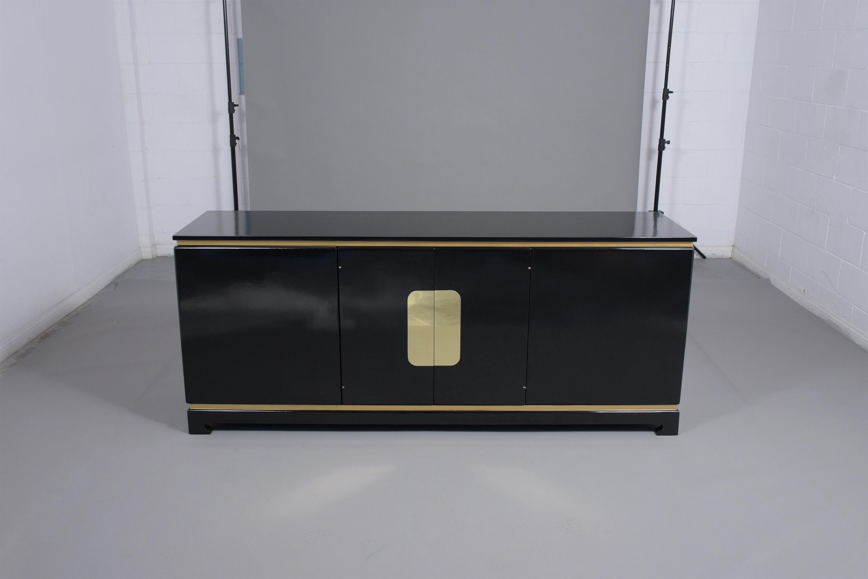 A vintage mid-century buffet hand-crafted out of wood stained in an elegant ebonized color with gild molding details and a newly lacquered finish. This fabulous commode has four doors with a large brass plate accent at the center doors, three