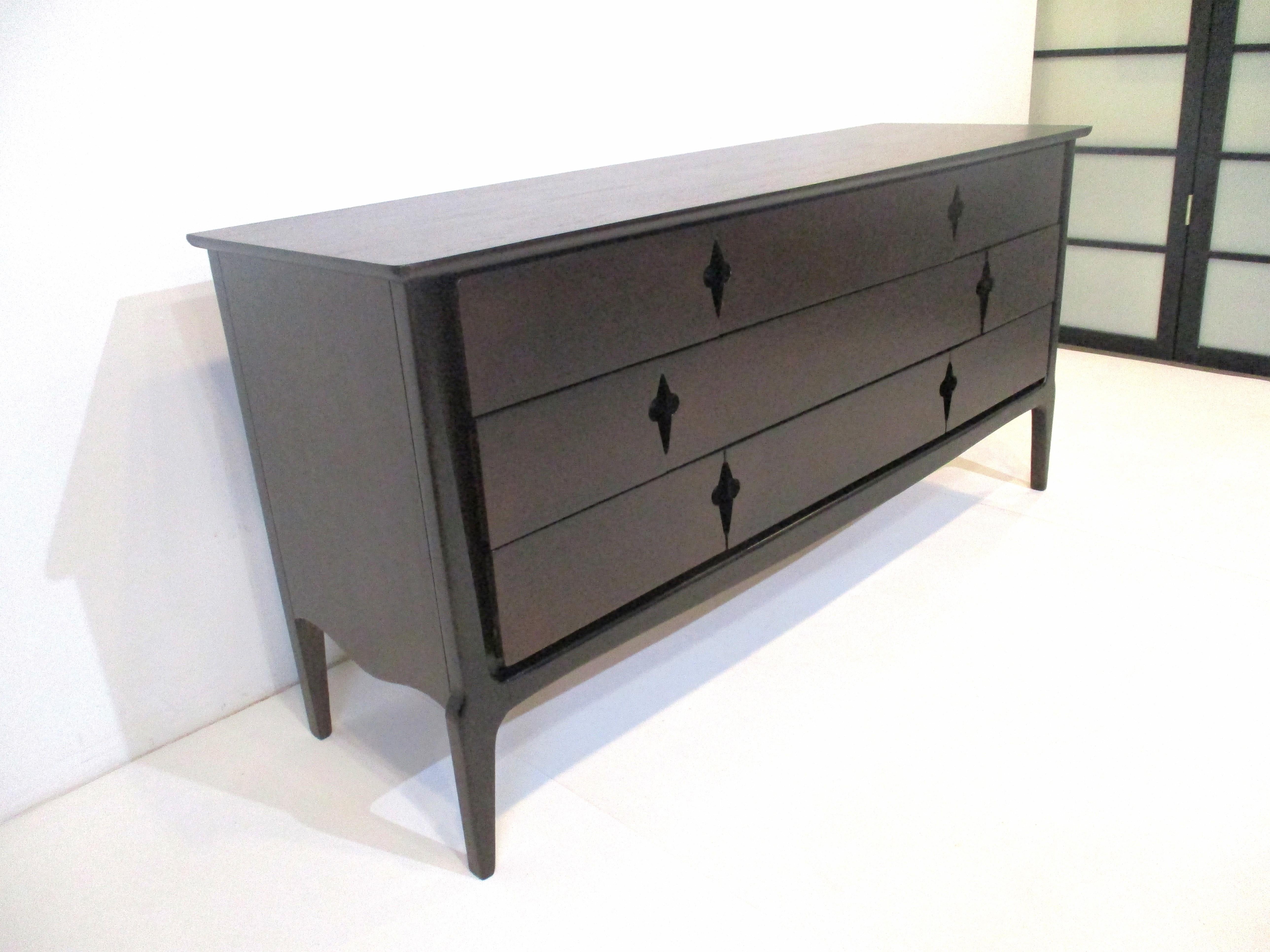 A ebony finished walnut nine drawer dresser chest with darker contrasting wood frame giving the piece a rich feel . The drawers have a midcentury de-lis fleur styled design as pulls , with tons of storage manufactured by the United Furniture company.