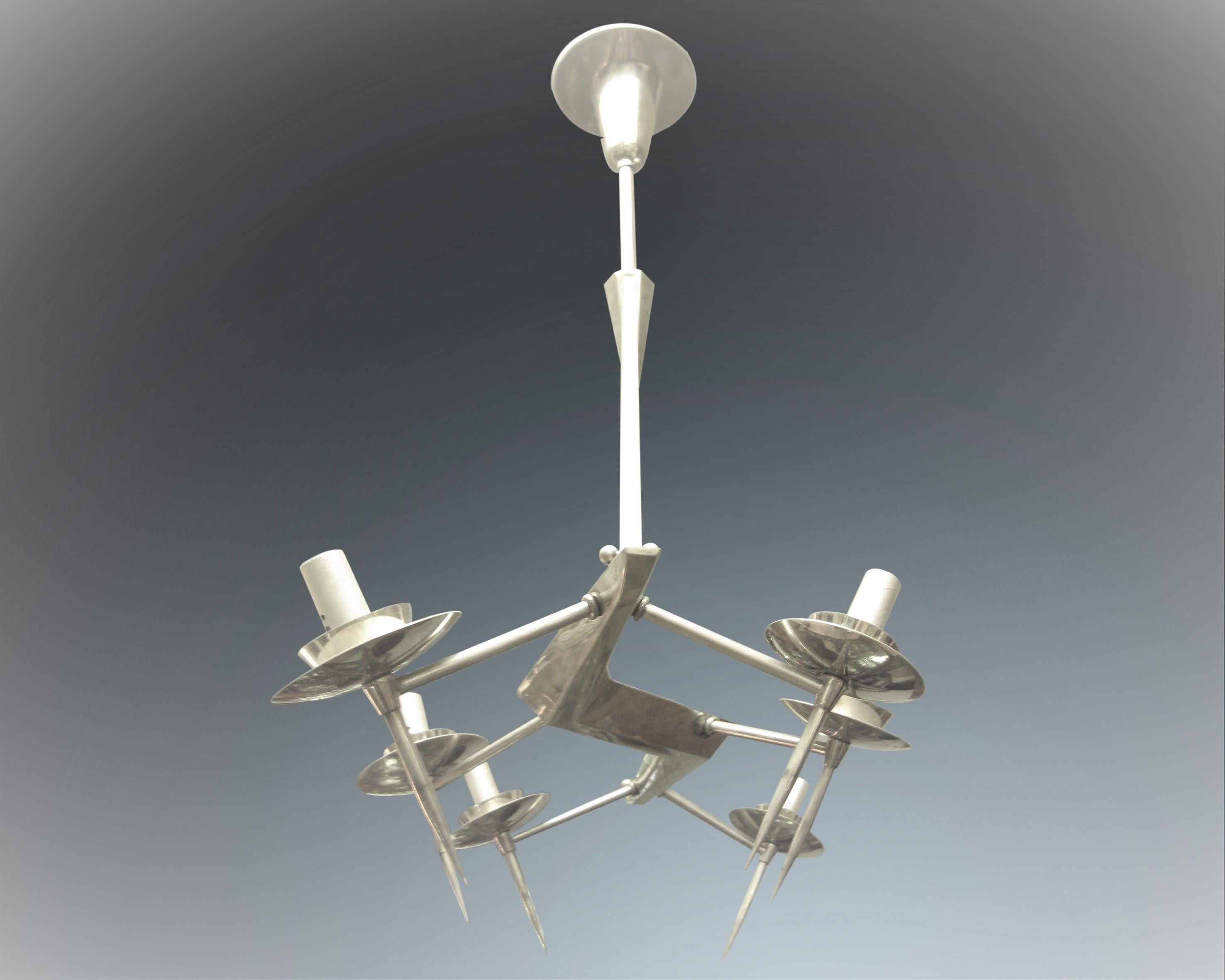 Un lampadario francese modernista in bronzo rivestito di nichel lucido, leggero e penetrante, caratterizzato da un'insolita sospensione triangolare a doppio braccio con sei luci incastonate in piatti riflettenti. I raggi del lampadario, ben fusi,