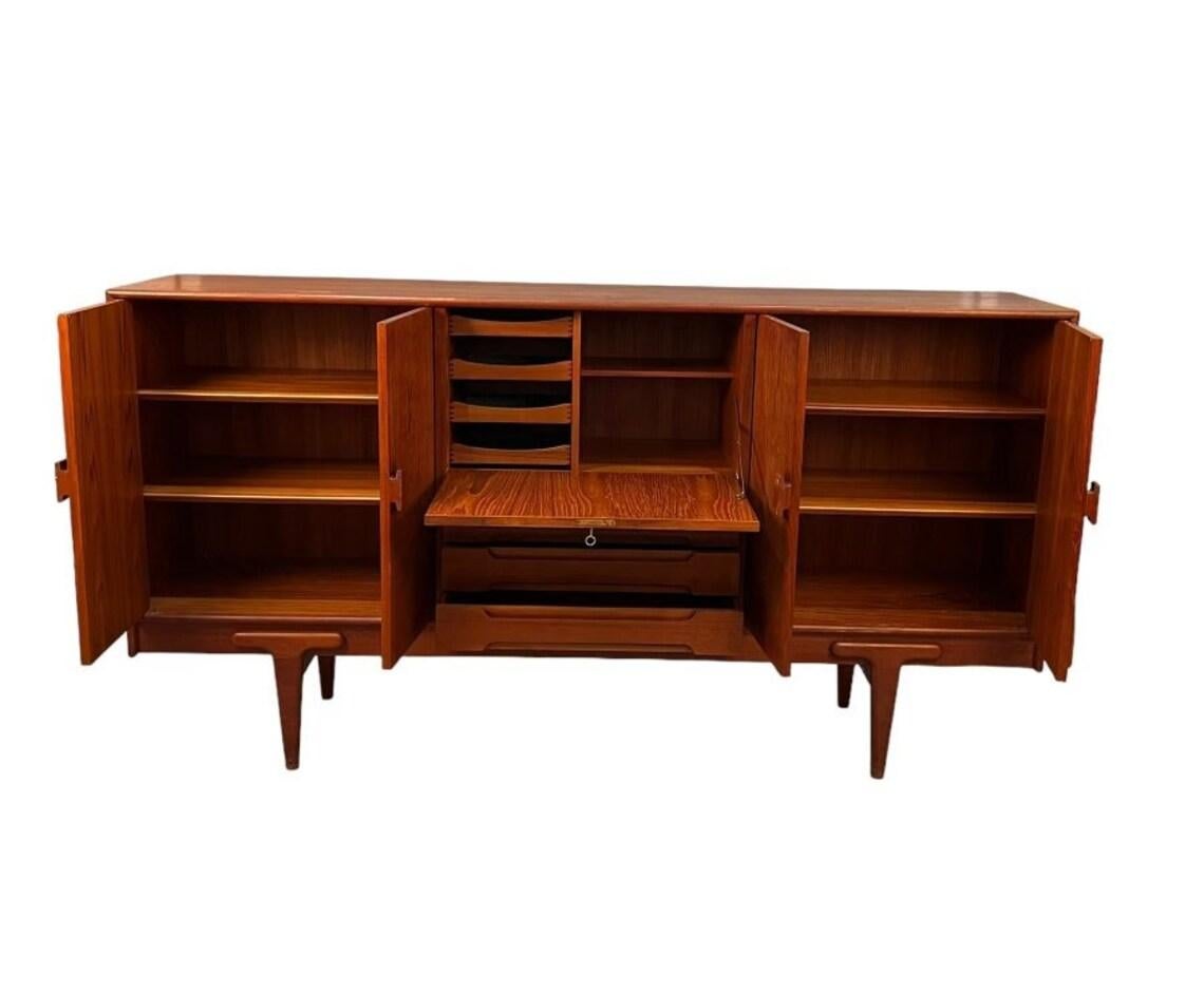 Mid-Century stunning tall teak sideboard with plenty of storage designed by Ejvind A. Johnson with middle desk section. 
Dimentions: L:84 D:18 H:44 inches