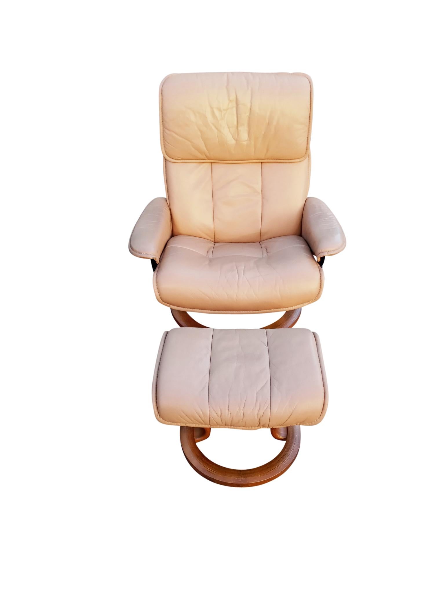 A Scandinavian style recliner and ottoman by Ekornes, their Stressless brand. With teak wood bases and metal frame and genuine leather upholstery, this is a comfortable sand color leather recliner on a round teak wood base that swivels 360 degrees.