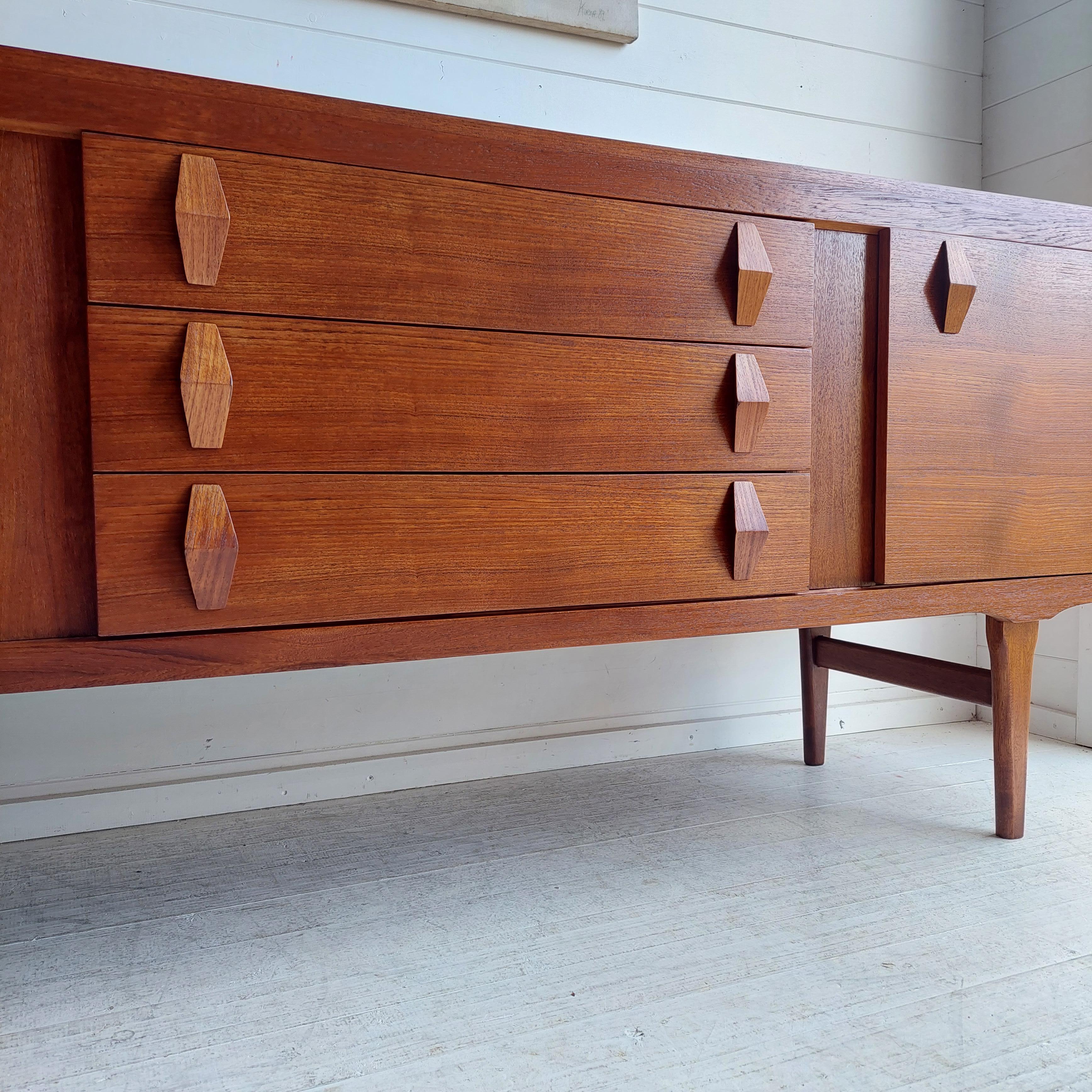 A superb vintage 60's/70's sideboard by Elliott's Of Newbury. from the 60s/70s
Finished in solid and veneered teak wood with beautiful grain patterns.
Sideboard with central bank of drawers and flanked by small single cupboard with geometric teak