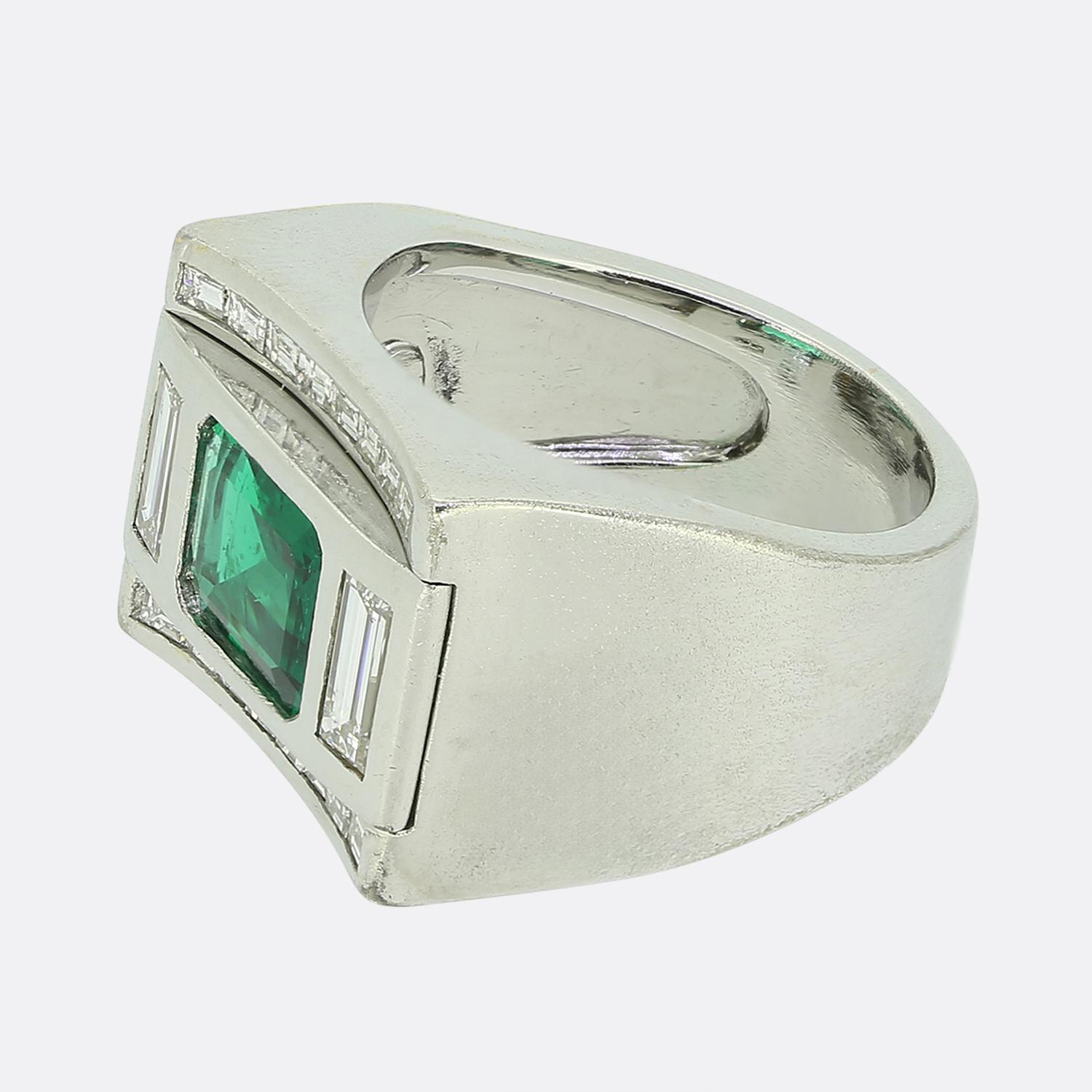 Hier haben wir einen massiven, aber dennoch stilvollen Smaragd- und Diamantring. Ein quadratischer Platinkopf beherbergt einen sattgrünen Smaragd mit transparentem Schliff in der Mitte des Gesichts. Dieser Hauptstein wird auf beiden Seiten von einem