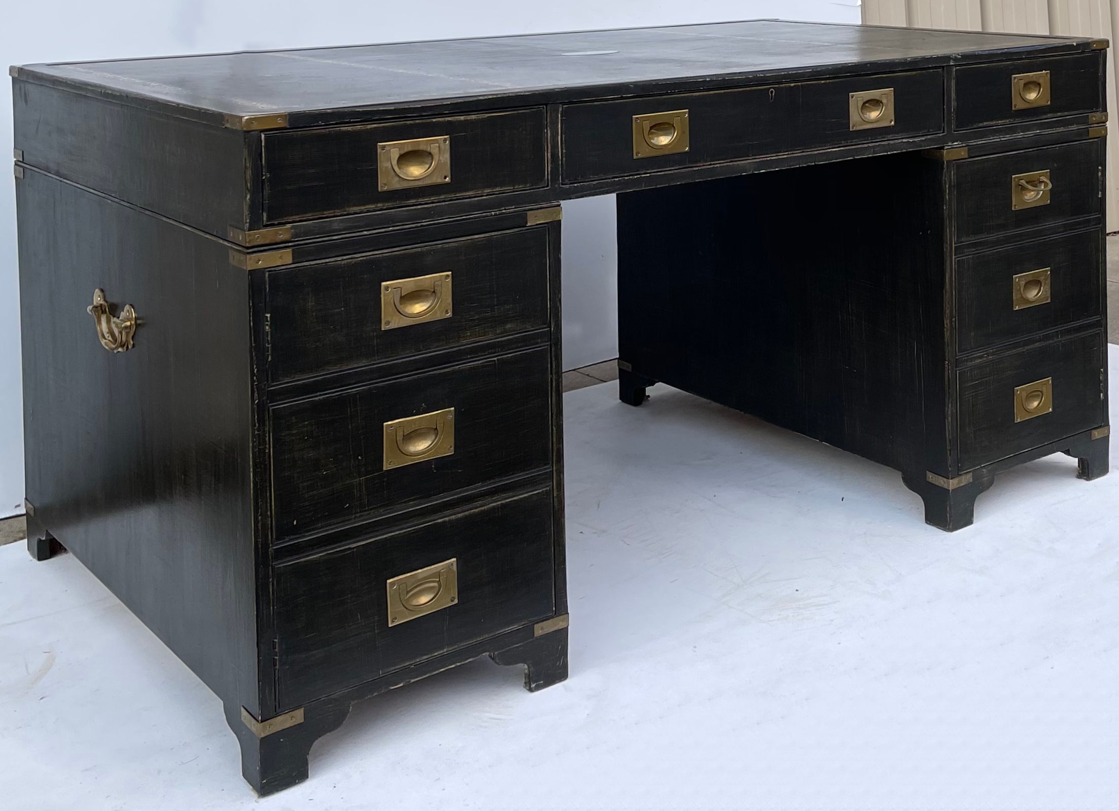 This is an English Bevan Funnell Ltd. campaign style partners desk. The top is a tooled green leather with light wear and brass plate. The finish is a custom aged and rubbed black. The piece includes cabinet style fronts, small drawers and one file