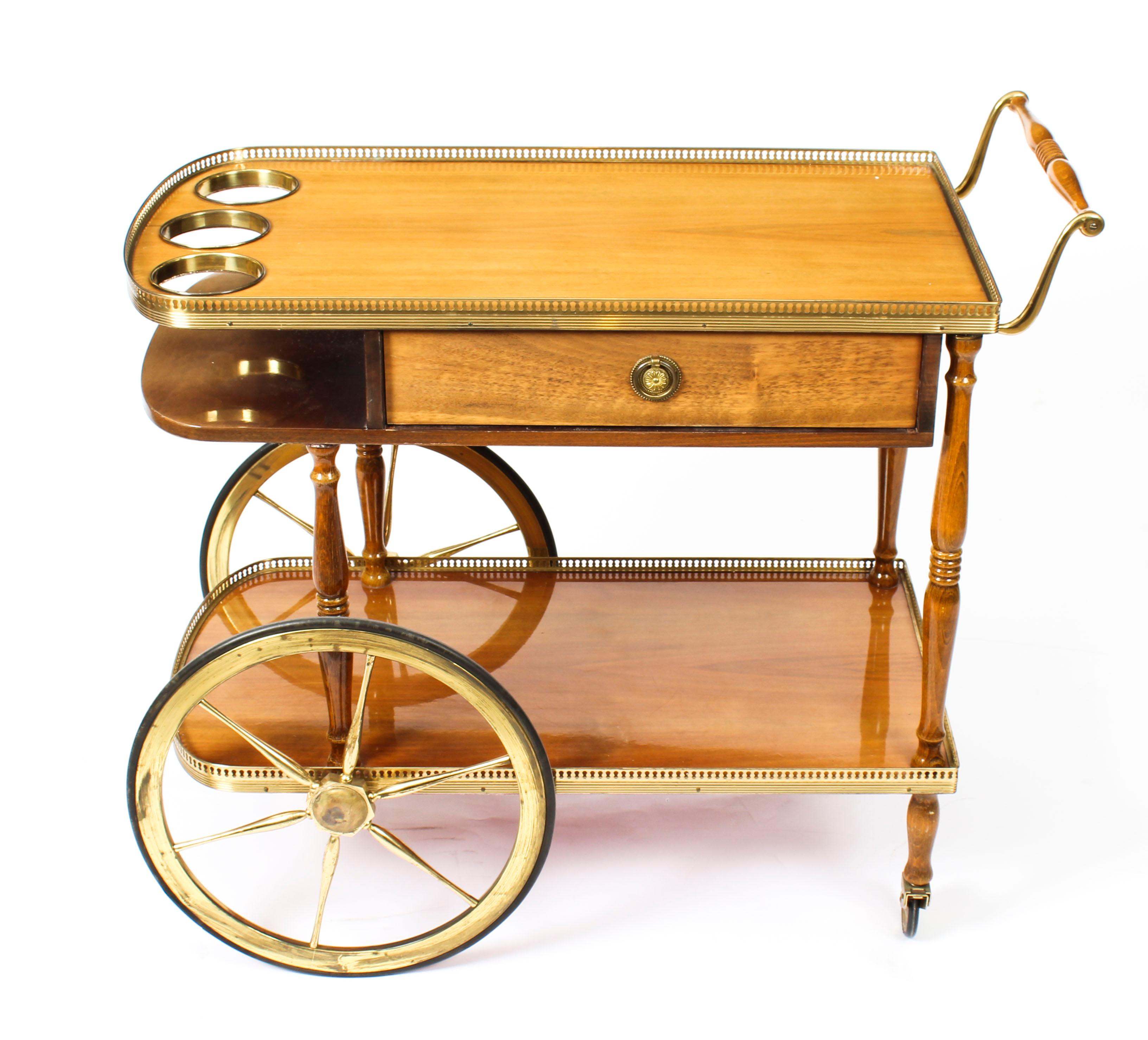 This is a very entertaining vintage birchwood midcentury drinks trolley circa 1960 in date.

The trolley features two levels with brass galleries joined by turned supports. The top gallery has a fitted three bottle holster and the frieze has a