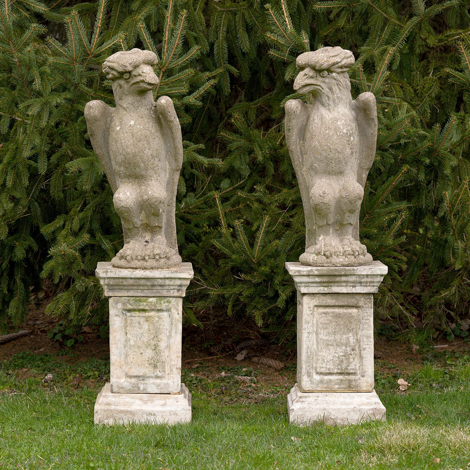 Paire d'oiseaux en pierre de composition sur piédestaux, les oiseaux ressemblant à des aigles mais avec des caractéristiques exagérées et stylisées, y compris des plumes de crête surdimensionnées et ondulées, les oiseaux debout regardant vers des