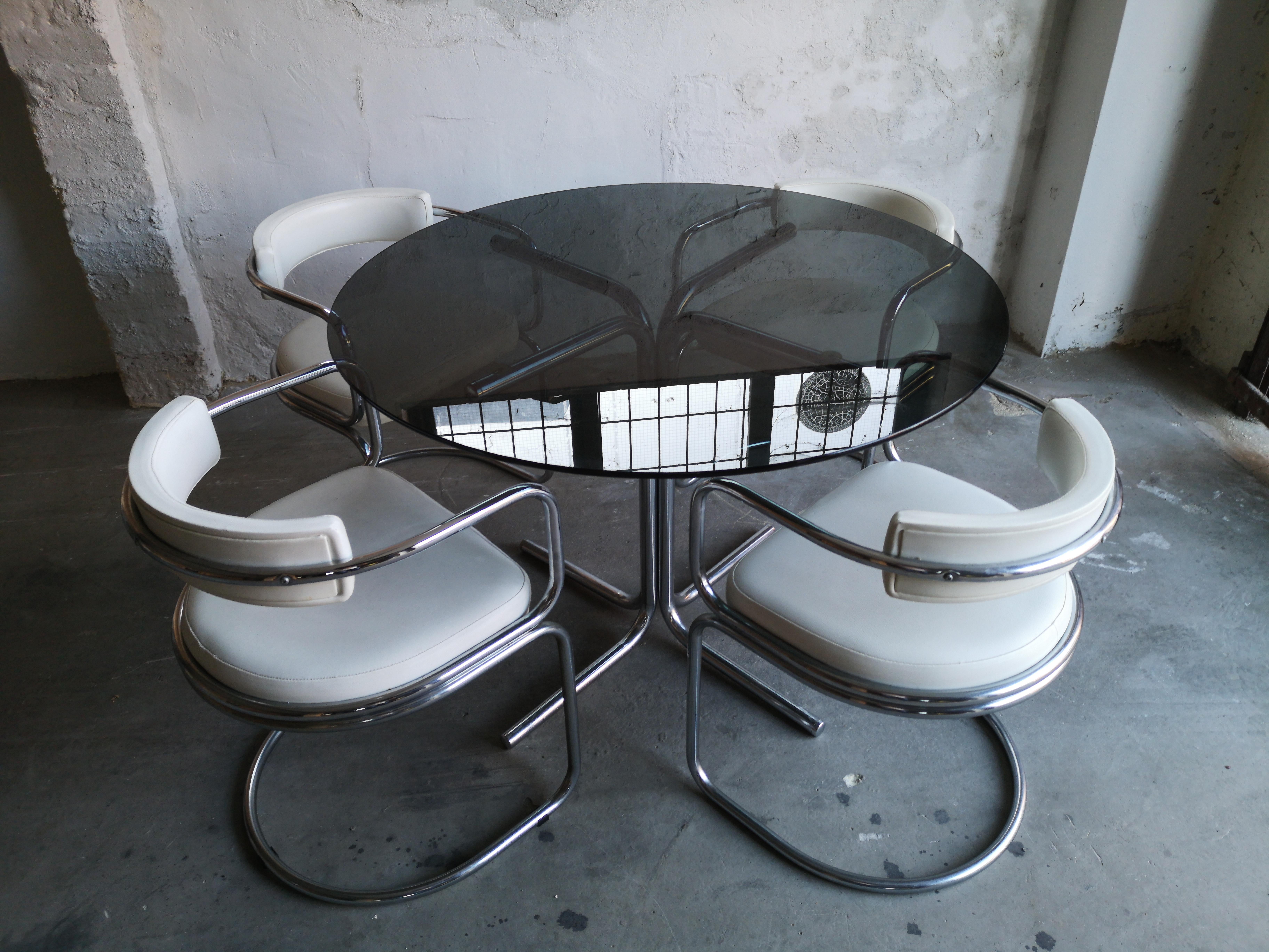 A lovely vintage tubular chrome and smoked glass dining set from circa 1970s. Very good vintage condition. All 4 chairs have original white vinyl upholstery with no rips or tears. There are hardly any signs of use on the glass top.