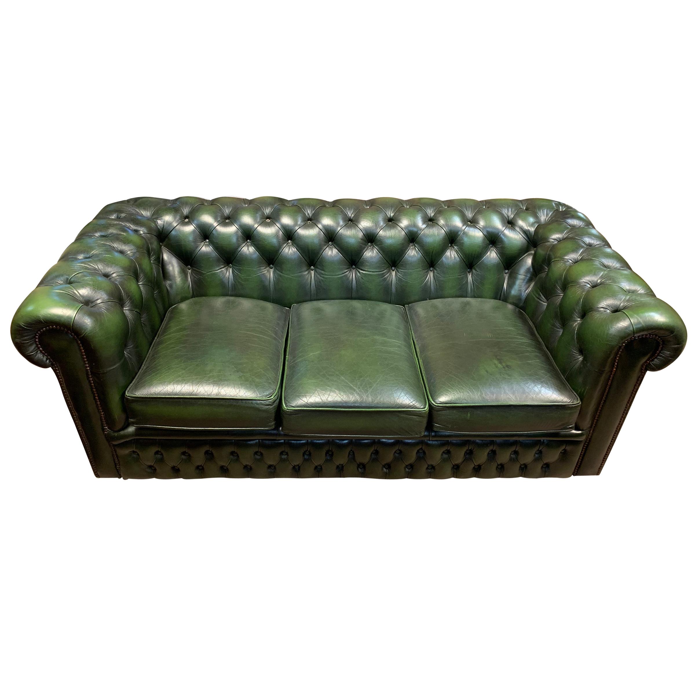 A quintessentially English mid-20th century emerald tufted chesterfield sofa with a rich dark emerald green leather upholstery with three cushions, rolled and tufted arms and back, and a tufted front panel, all with brass nailhead trim. The sofa