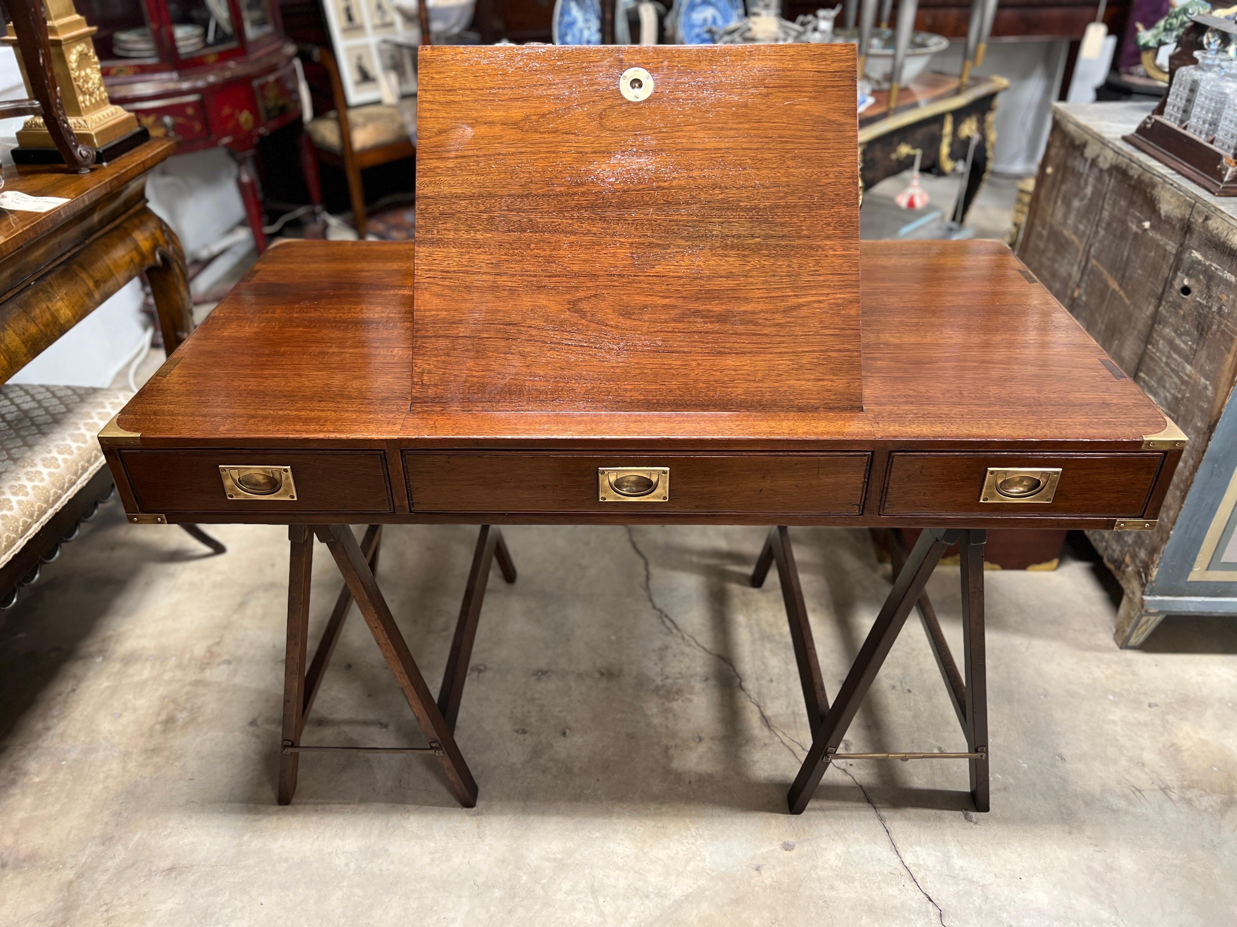 English, mid century.

A beautiful English campaign desk in the military style, having two collapsible trestle bases. The from has 3 drawers with original polished brass handles. The sides with fitted and recessed handles for easy transportation and