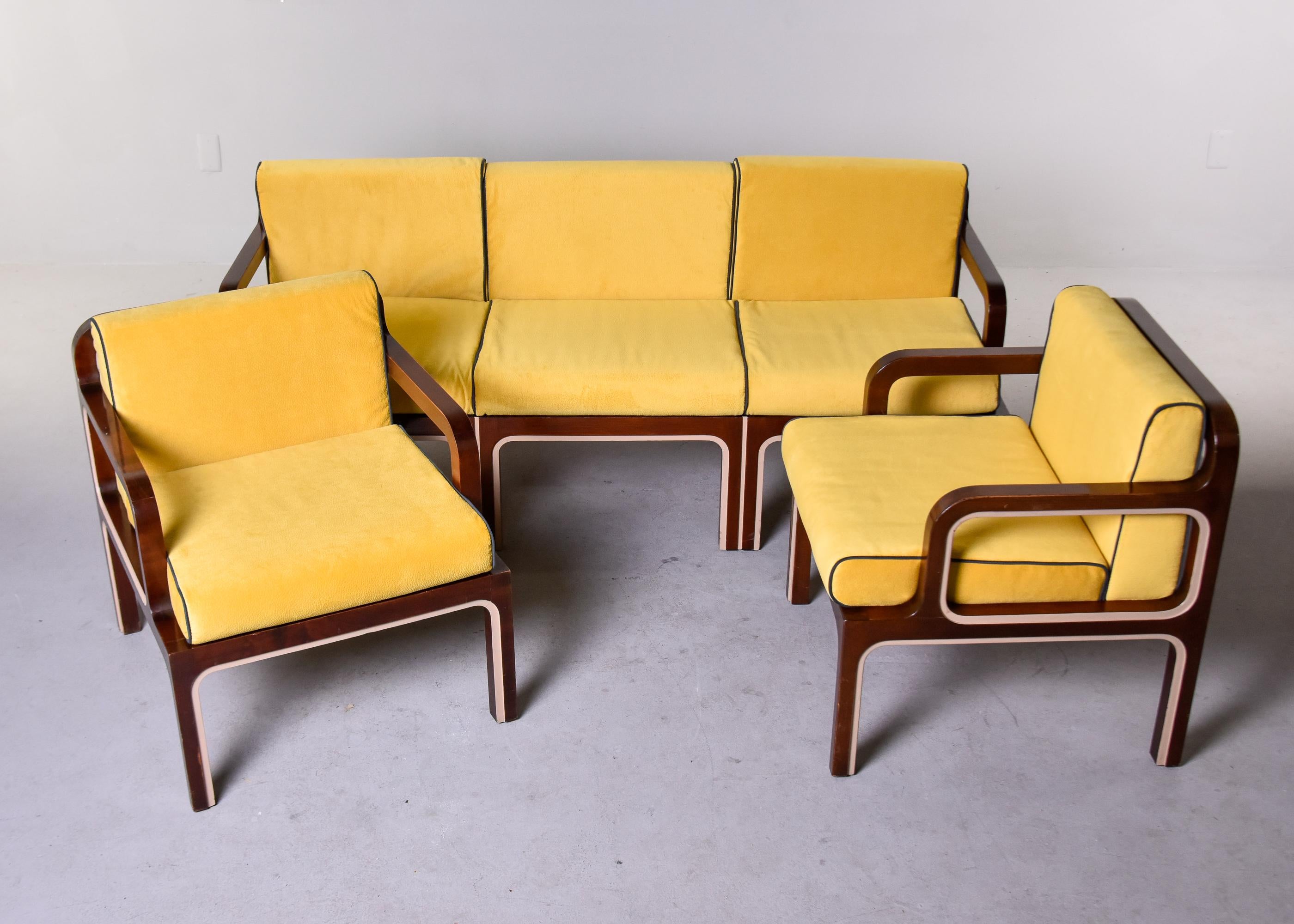 This sofa and pair of chairs is from London and dates from the early 1970s. All three pieces were newly upholstered in a gold moleskin fabric with black welting by the European dealer we acquired the set from. Dark wood frames have a lacquered