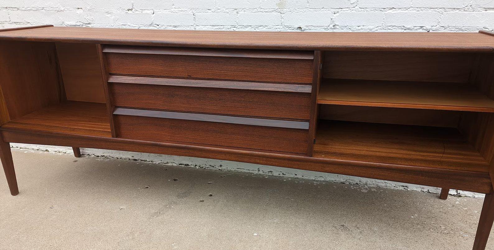 Mid Century English Modern Teak Credenza by Younger
 
Above average vintage condition and structurally sound. Has some expected slight finish wear and scratching. Top has been refinished and does not have original finish. Back in piece is finished