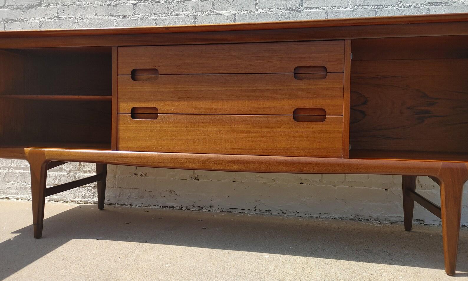 Mid Century English Modern Teak Sideboard by Younger
 
Above average vintage condition and structurally sound. Has some expected slight finish wear and scratching. Top has a couple discolorations and front edge has some slight dings. Outdoor listing