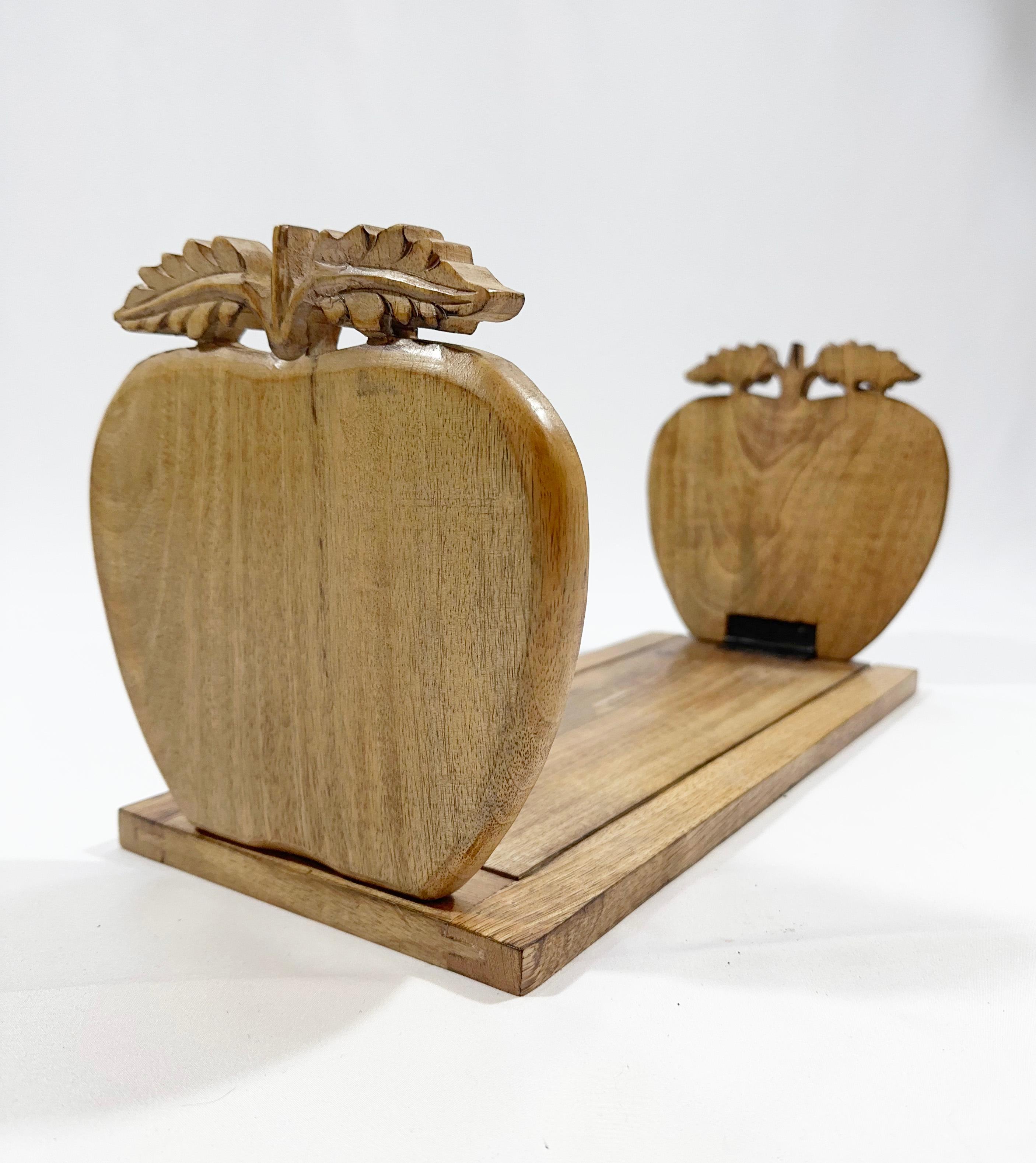 This mid-century book slide, originating from England, is a quaint amalgamation of utility and caprice. Handcrafted from English oak, known for its endurance and patina that deepens with age, it features whimsically carved apple-shaped book ends, a
