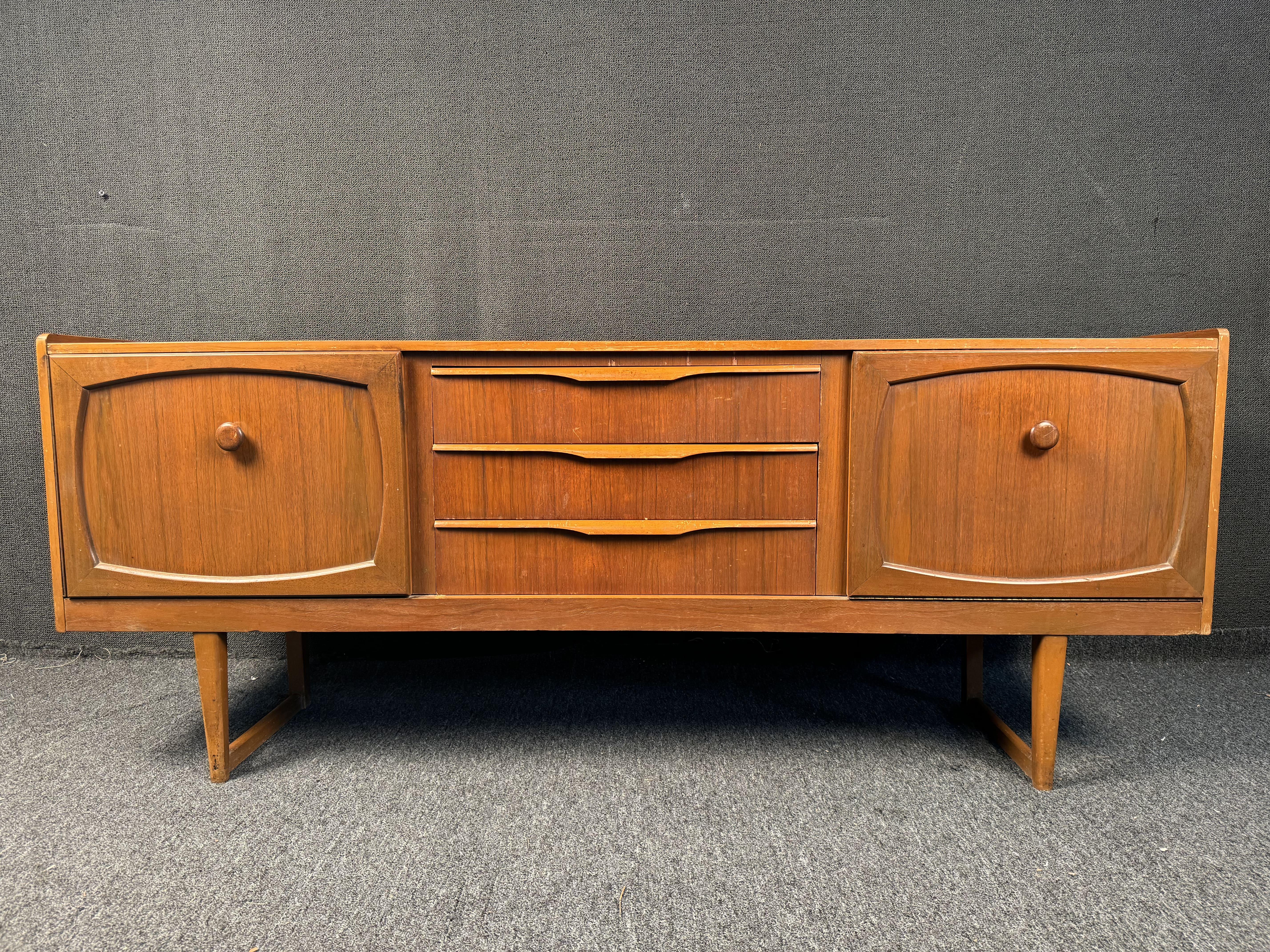 Grazie all'artigianato britannico del dopoguerra e all'influenza del design moderno scandinavo, questa bellissima credenza inglese in teak offre davvero il meglio dei due mondi! Con le sue gambe a slitta splendidamente intagliate che conferiscono