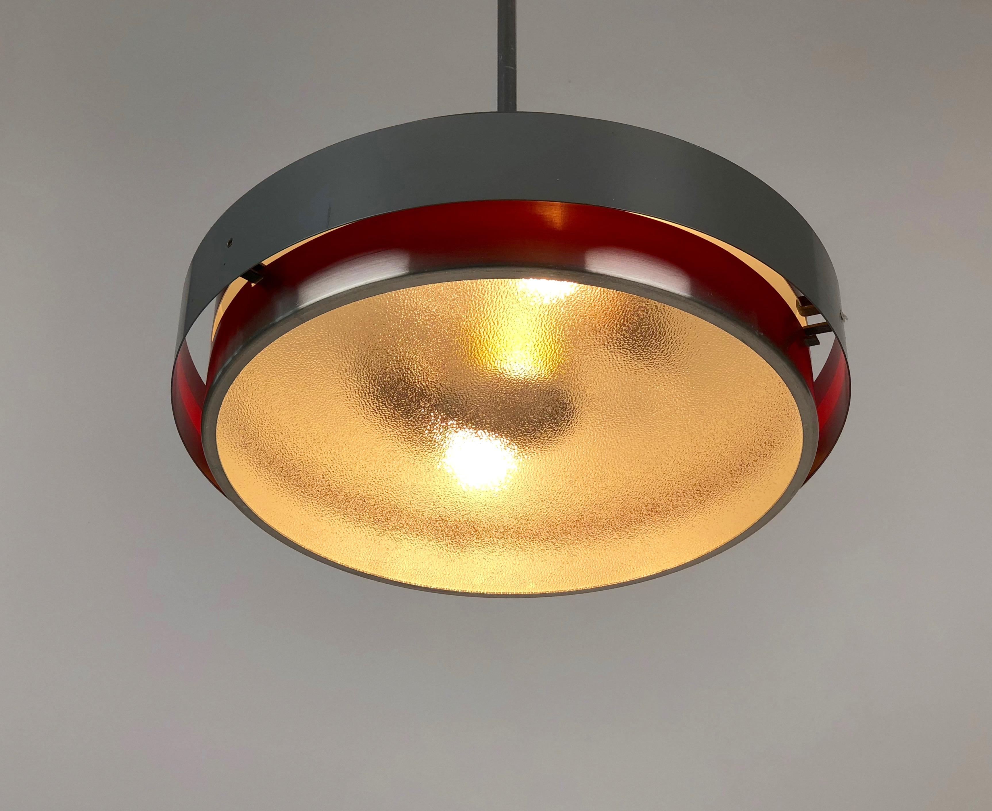 Simple pendant-lamp made in aluminium with satin glass disc.
The equator is outside grey and inside red lacquered, this effect is visible when the lamp is illuminated.
The lamp is in a very good condition.